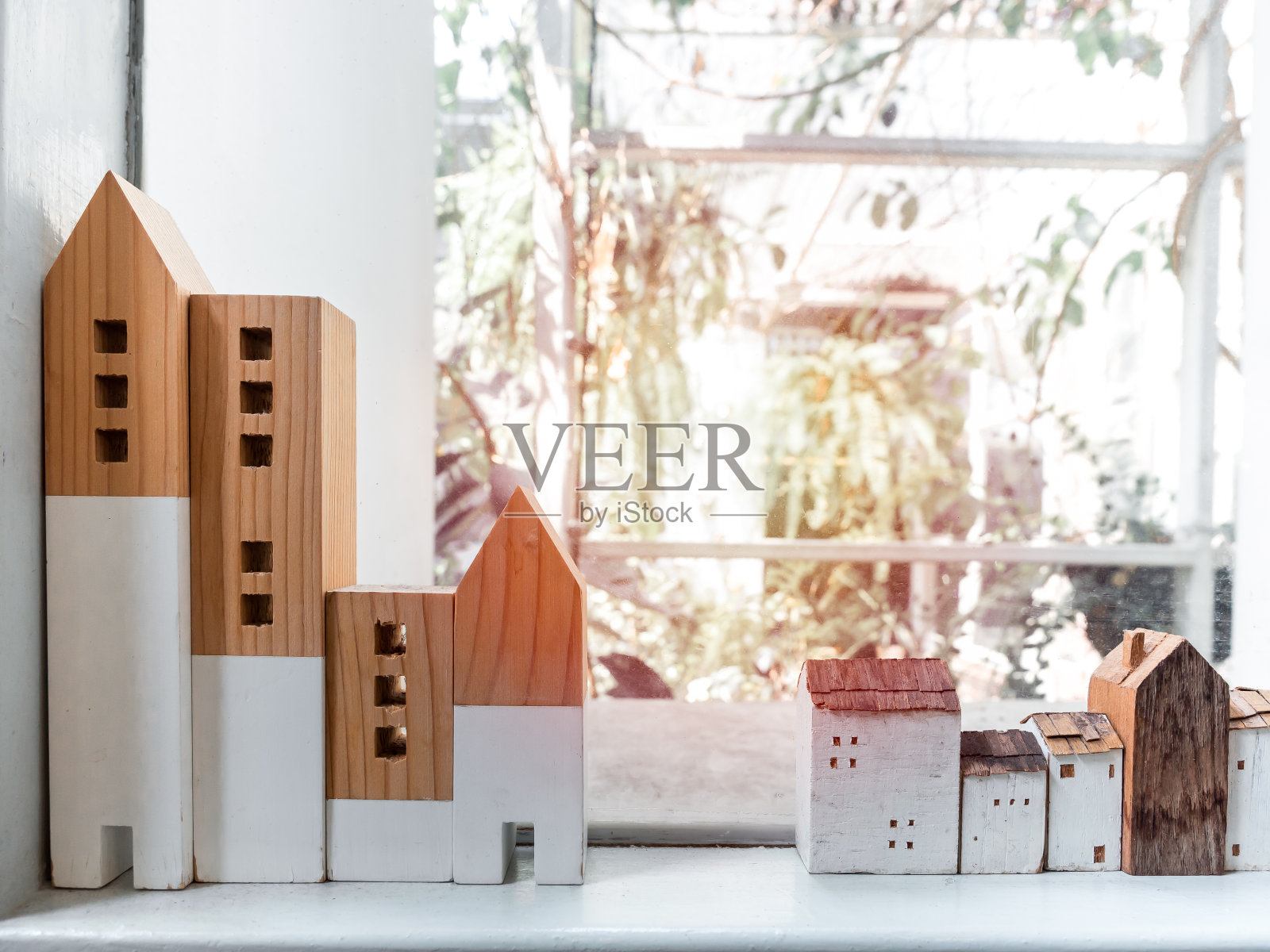 在窗户玻璃附近的白色架子上的微型木房子有阳光。照片摄影图片