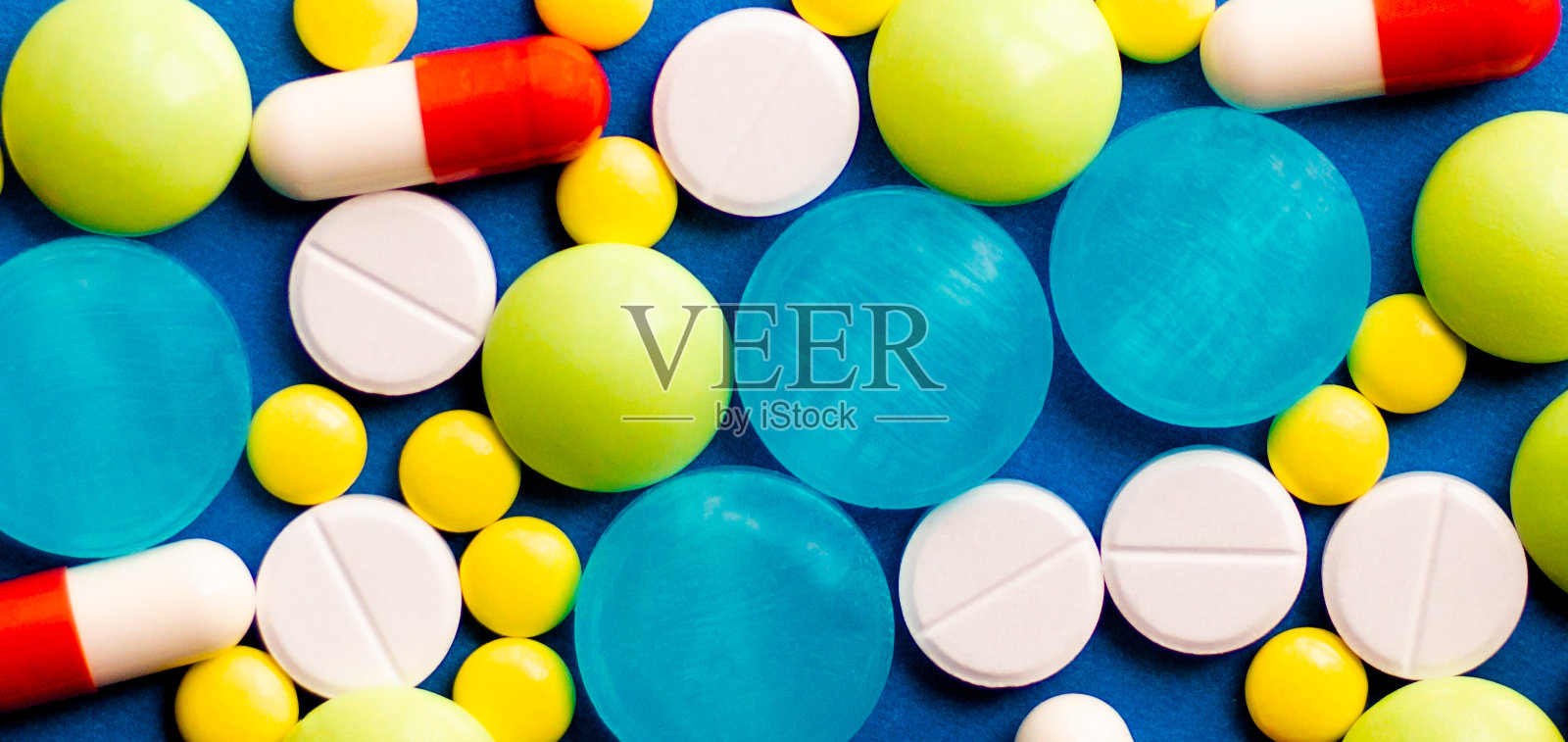 在蓝色的背景上洒了彩色的药物和药片。药理学和医学为健康而斗争。药物成瘾。各种疾病的治疗照片摄影图片
