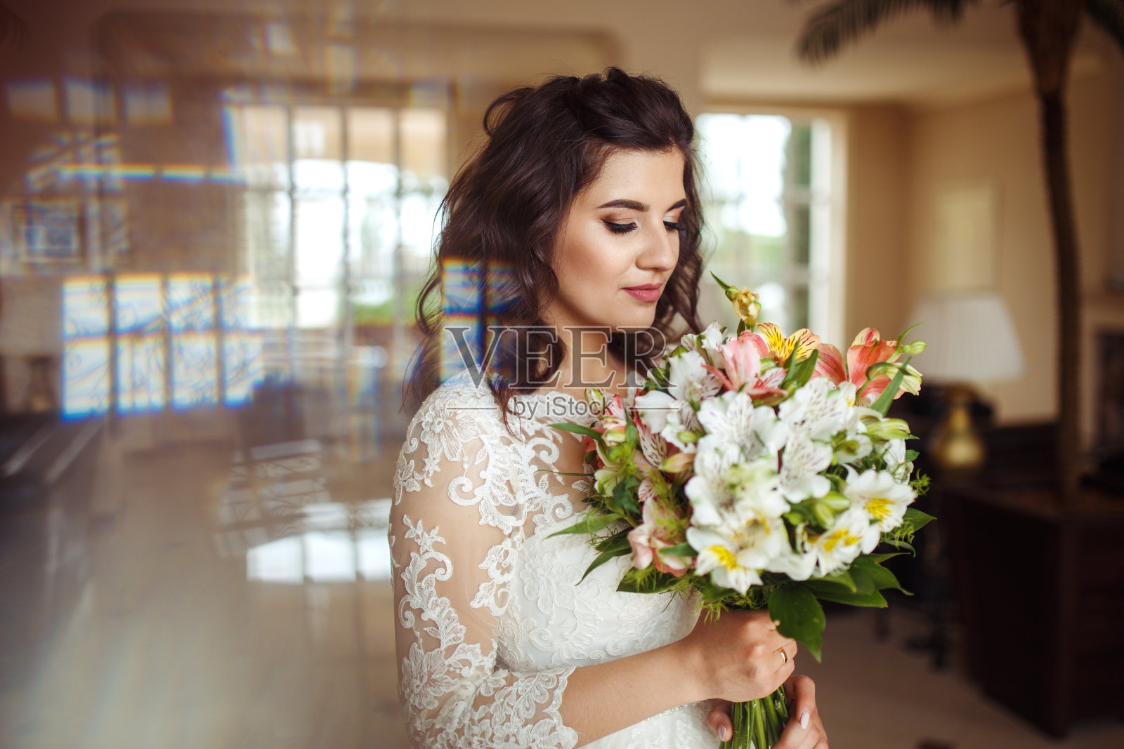 一位美丽的新娘身穿白色婚纱，手捧一束鲜花，在一家美丽的酒店里摆姿势。照片摄影图片