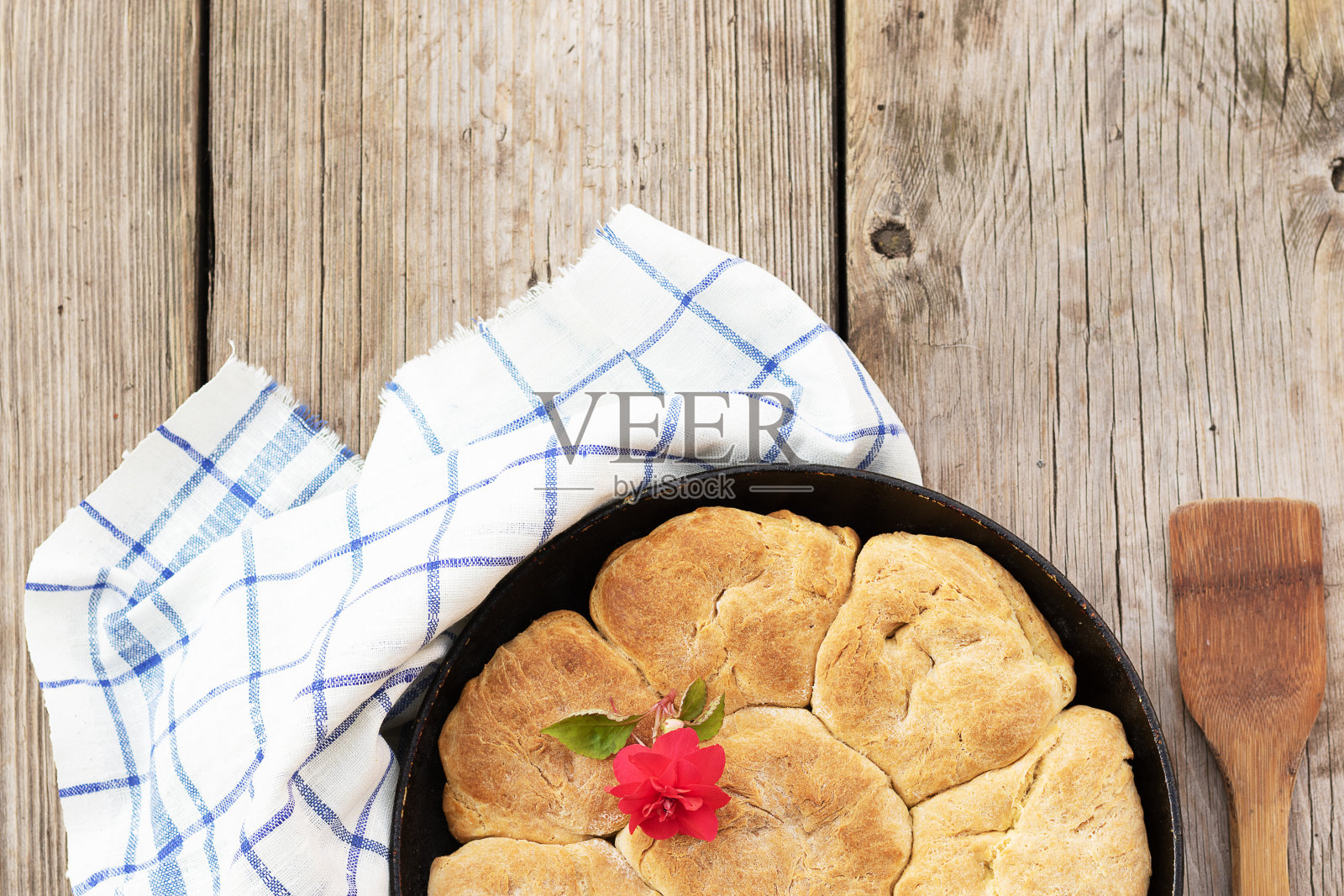 新鲜的自制全麦面包放在金属烤盘里。一个小红花装饰馒头。木制的背景，布餐巾和抹刀放在旁边照片摄影图片