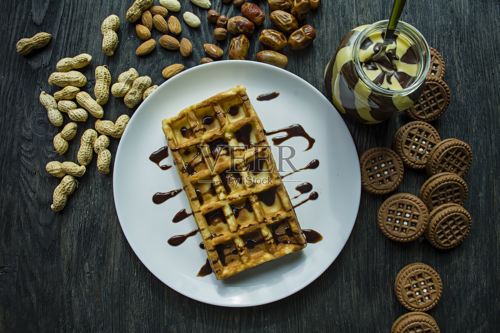 传统的比利时华夫饼，在深色木质背景上覆盖巧克力。美味的早餐。装饰以坚果，坚果糊。照片摄影图片