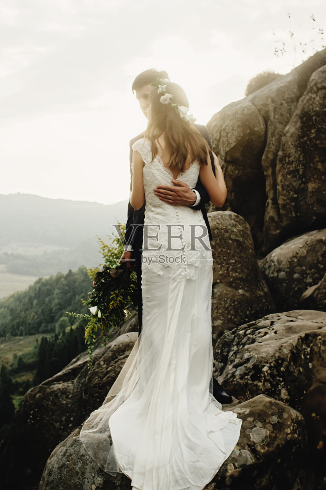 时髦华丽的新婚夫妇站在岩石在傍晚的光山照片摄影图片