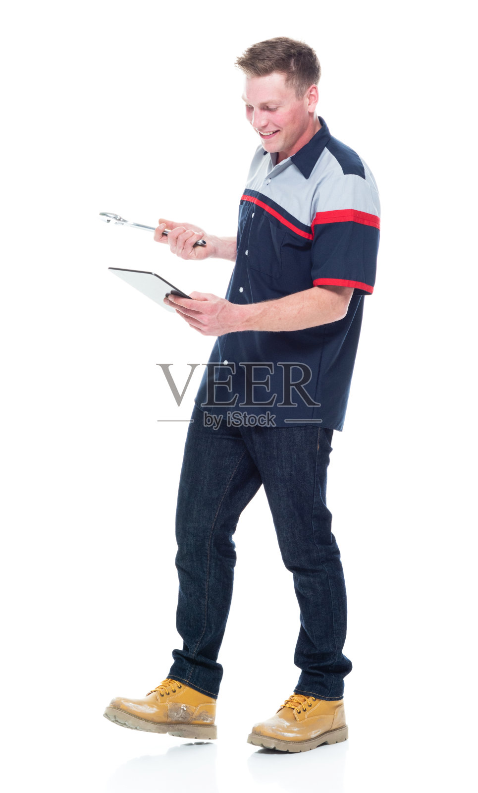 白人年轻男性修理工穿着制服站在白色背景前，手持开口扳手，使用数码平板电脑照片摄影图片