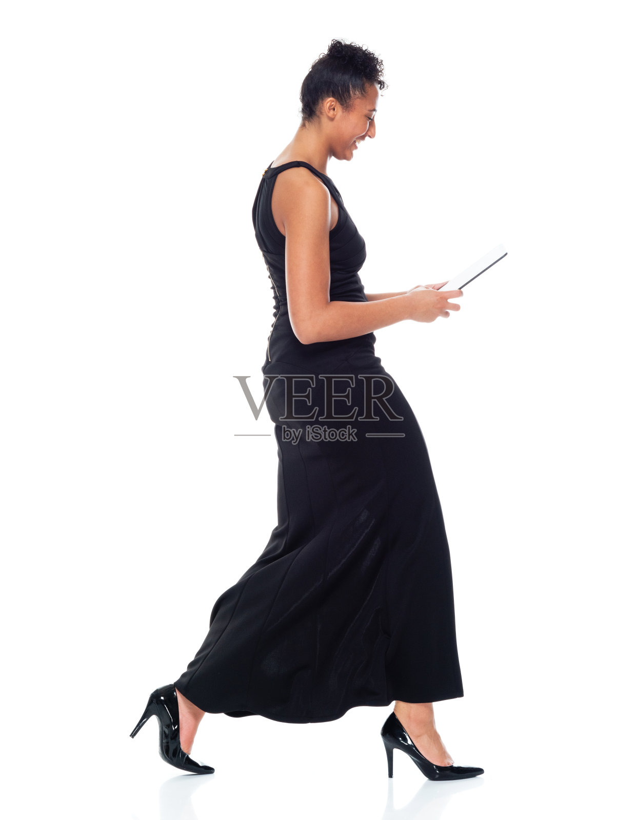 非洲裔年轻女性穿着裙子，使用平板电脑走在白色背景前照片摄影图片