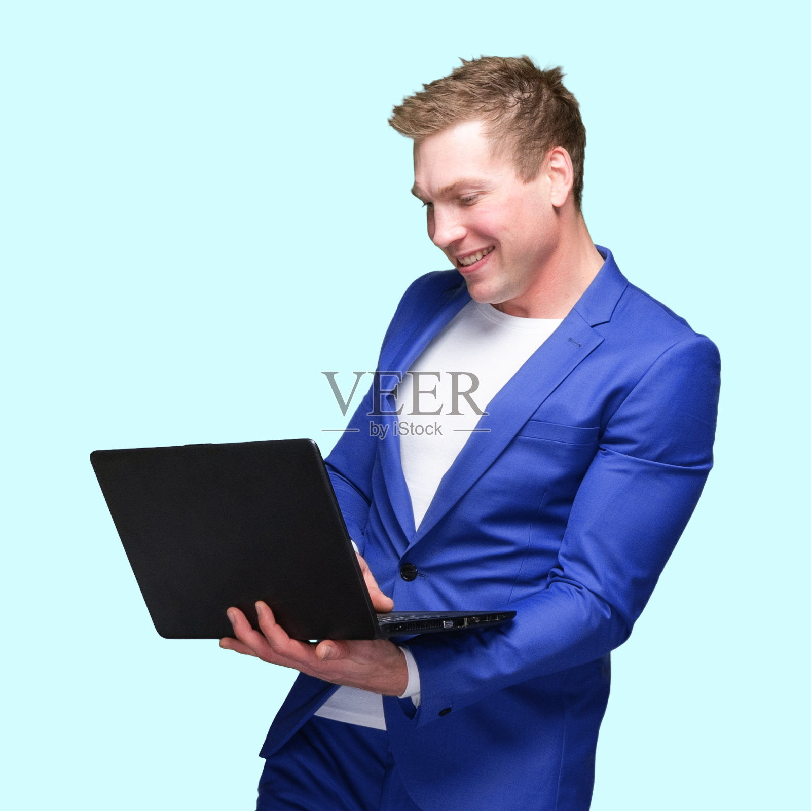 白人年轻男性站在蓝色背景下，穿着智能便服，使用电脑照片摄影图片