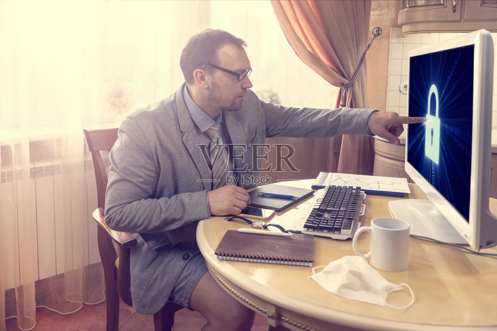 坐在餐桌旁，一个穿着西装和短裤的年轻人在社交网络上远程工作，商人解锁电脑，区块链技术概念照片摄影图片