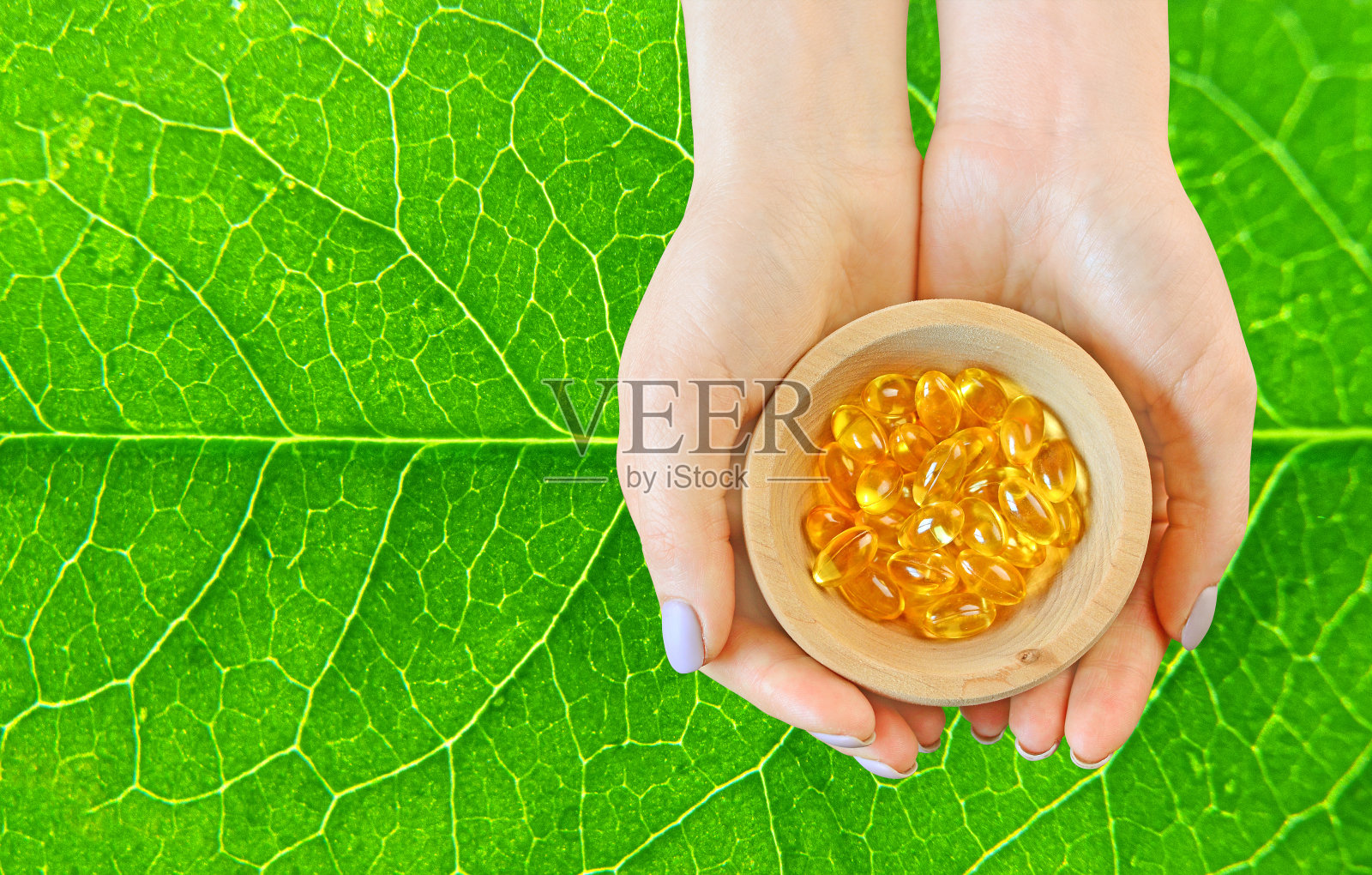 顺势疗法的概念。天然草药维生素。女孩双手拿着盛满维他命胶囊的木盘放在绿叶上。照片摄影图片