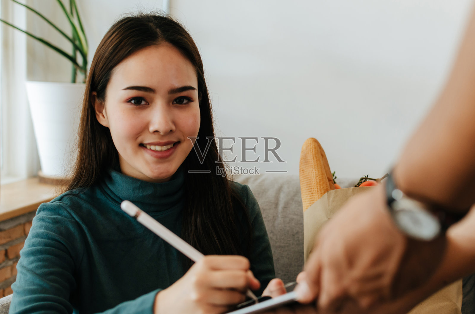 漂亮女人客户看相机得到笔形式的快递服务人员签字在数字手机平板接收包袋新鲜食品在家，快递和网上购物的概念照片摄影图片