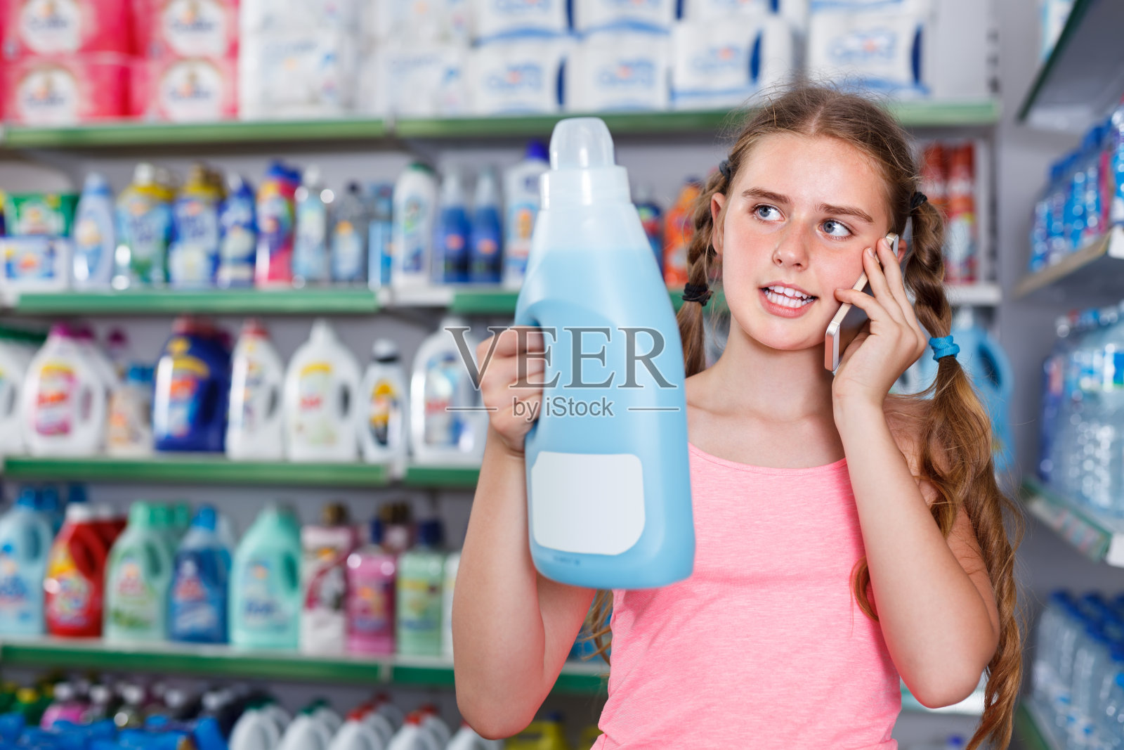在超市里，集中注意力的少女一边打电话，一边看装有家用化学药品的瓶子照片摄影图片