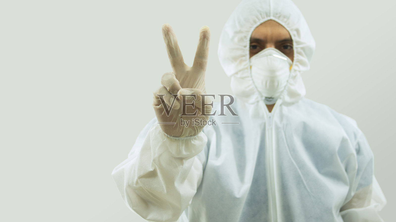 医生戴着口罩，穿着生物防护服，手臂向前伸，右手在白色背景上做出和平和爱的手势照片摄影图片