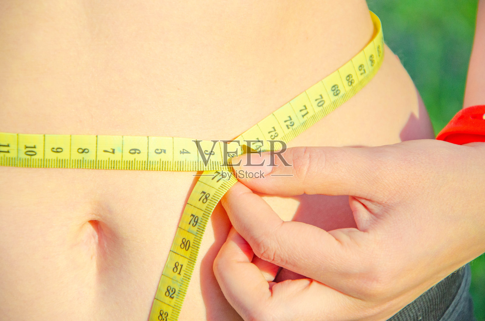 女孩量了量她的腰，一个黄色厘米的漩涡。胖胖的肚子，皱褶的脂肪。运动，适当的营养，减肥。照片摄影图片