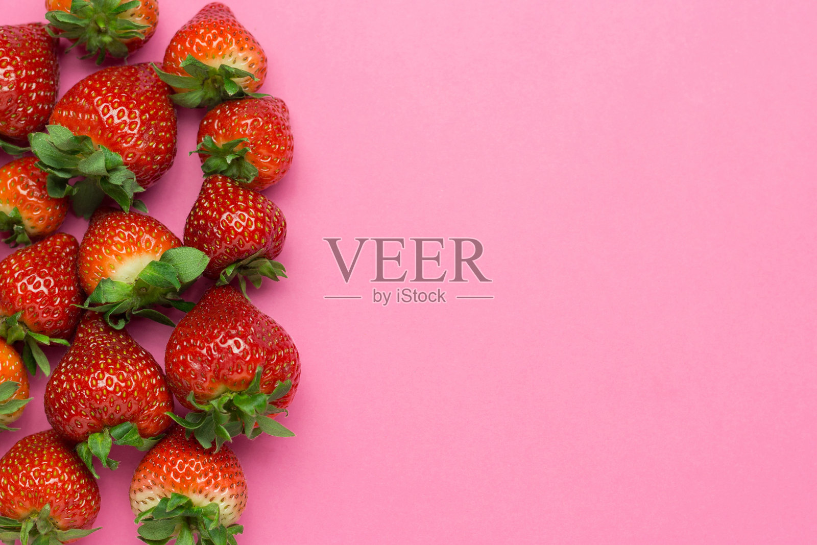 粉红色背景上放着成熟多汁的草莓。图案，新鲜浆果平铺。创意简约的食物概念。本空间照片摄影图片
