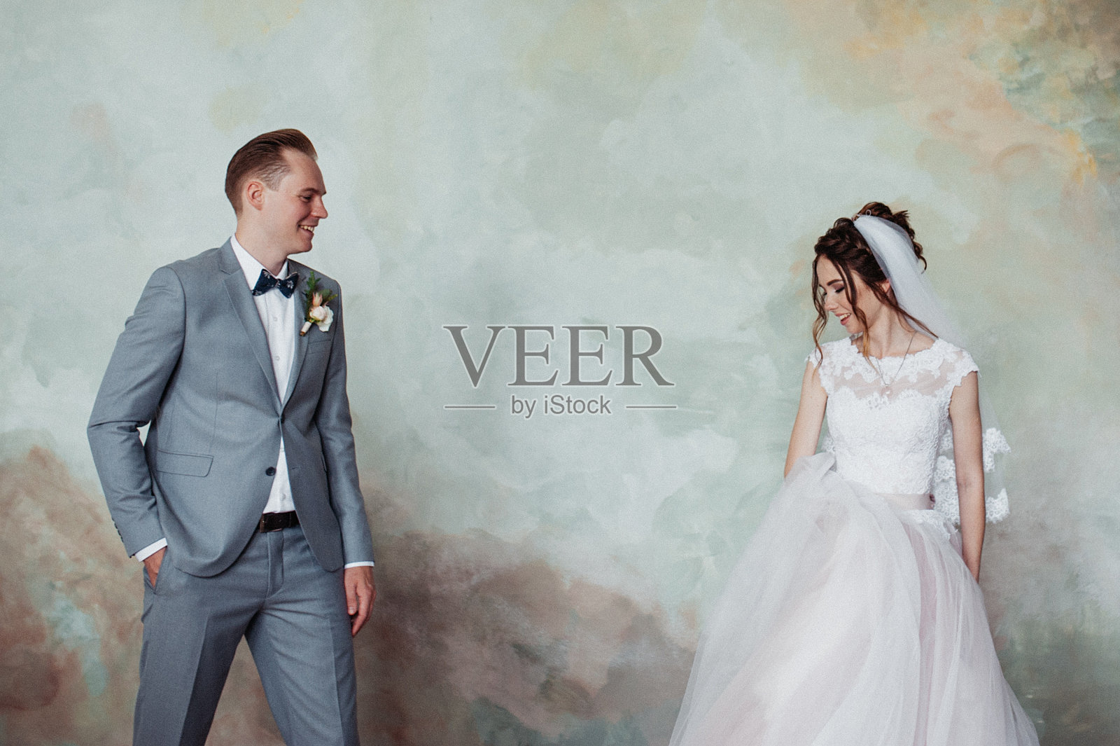 第一次会议。新郎捧着一束花走进新娘的房间。他们拥抱和亲吻。粉色婚纱，灰色套装，时尚的花束。照片摄影图片