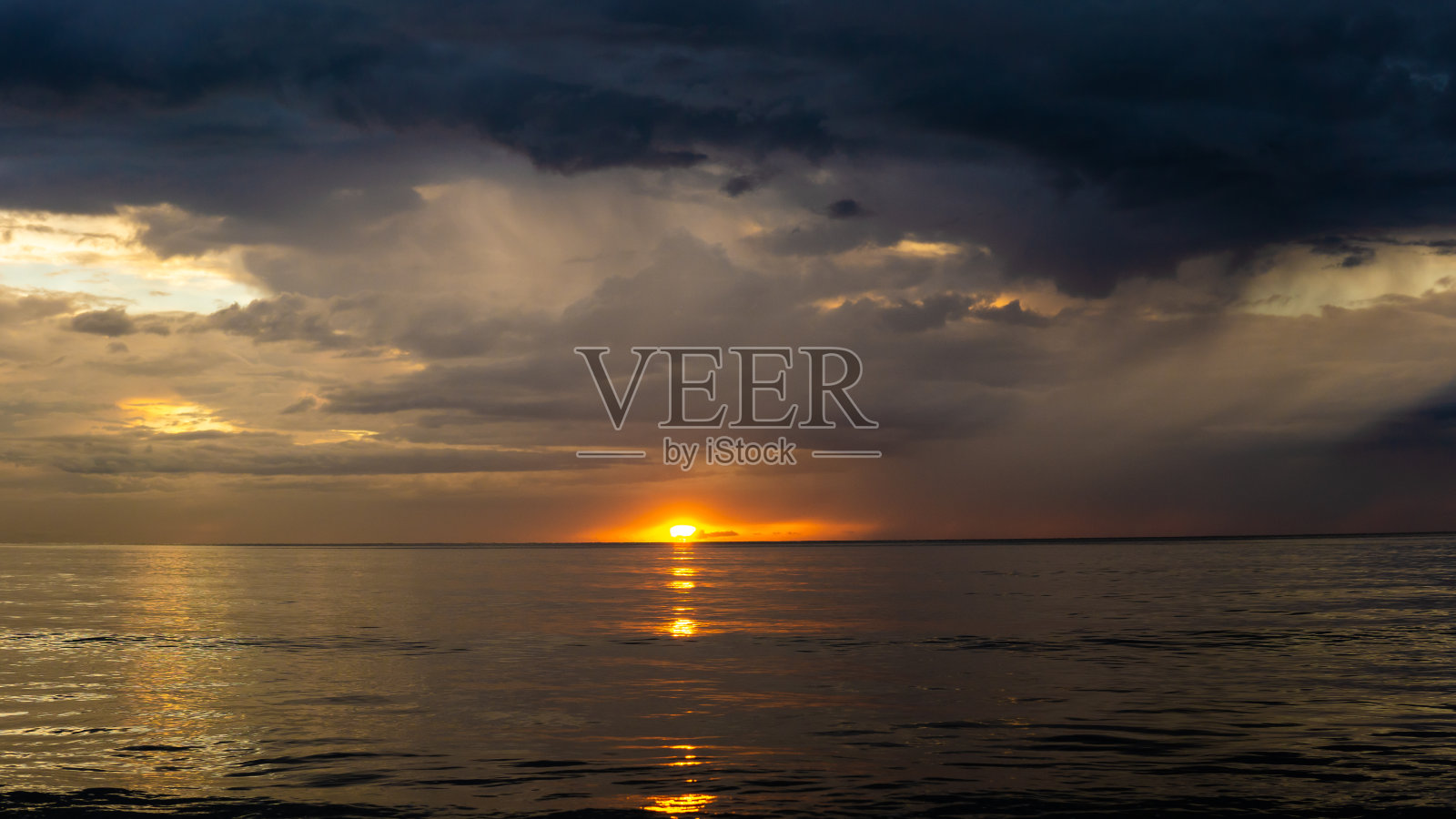 沙巴州丹戎阿鲁海滩黄昏时的日落，深蓝色的天空和橙色的太阳反射在海水上。照片摄影图片