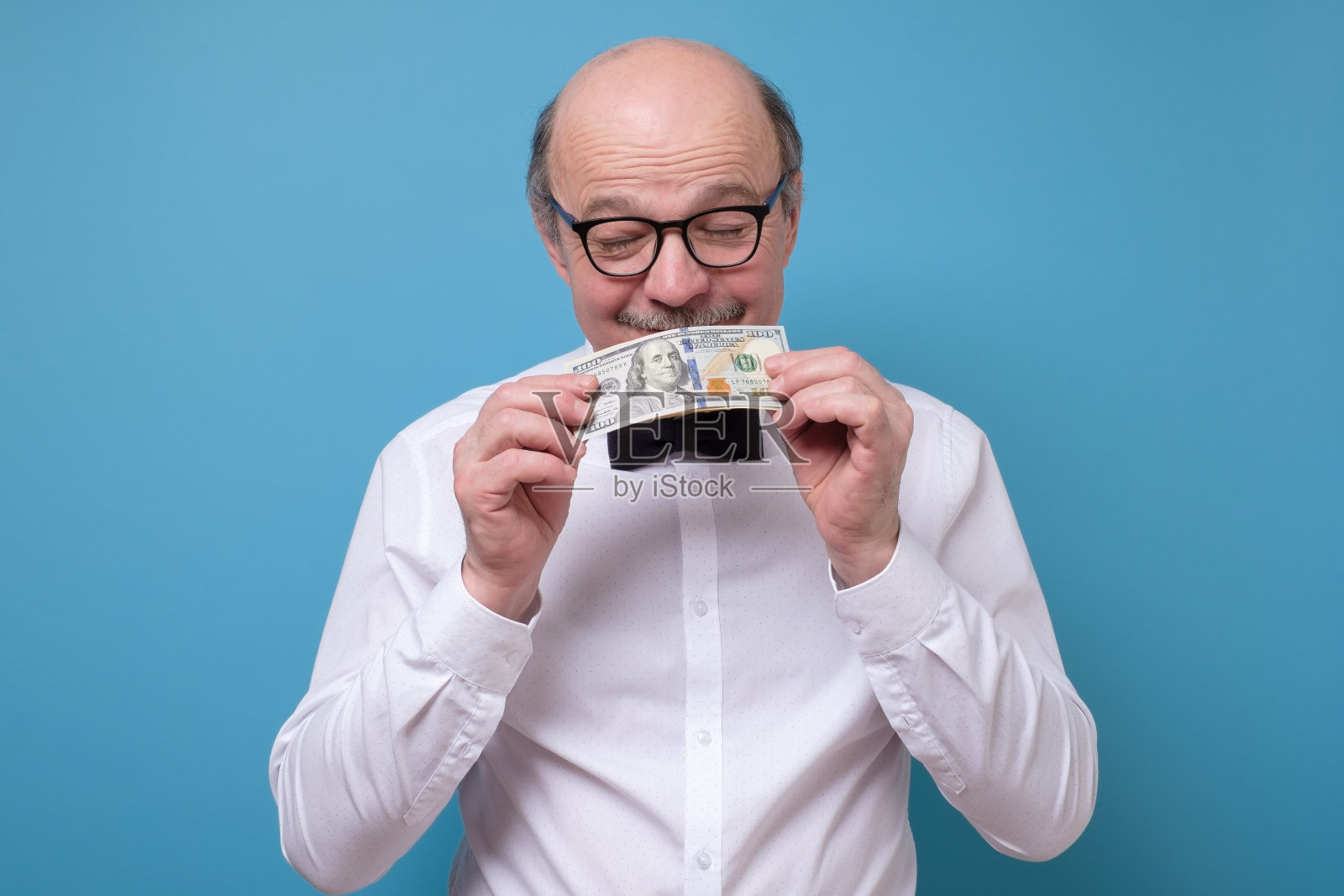 戴眼镜的资深白人男子拿着一张一美元的钞票，闻了闻照片摄影图片