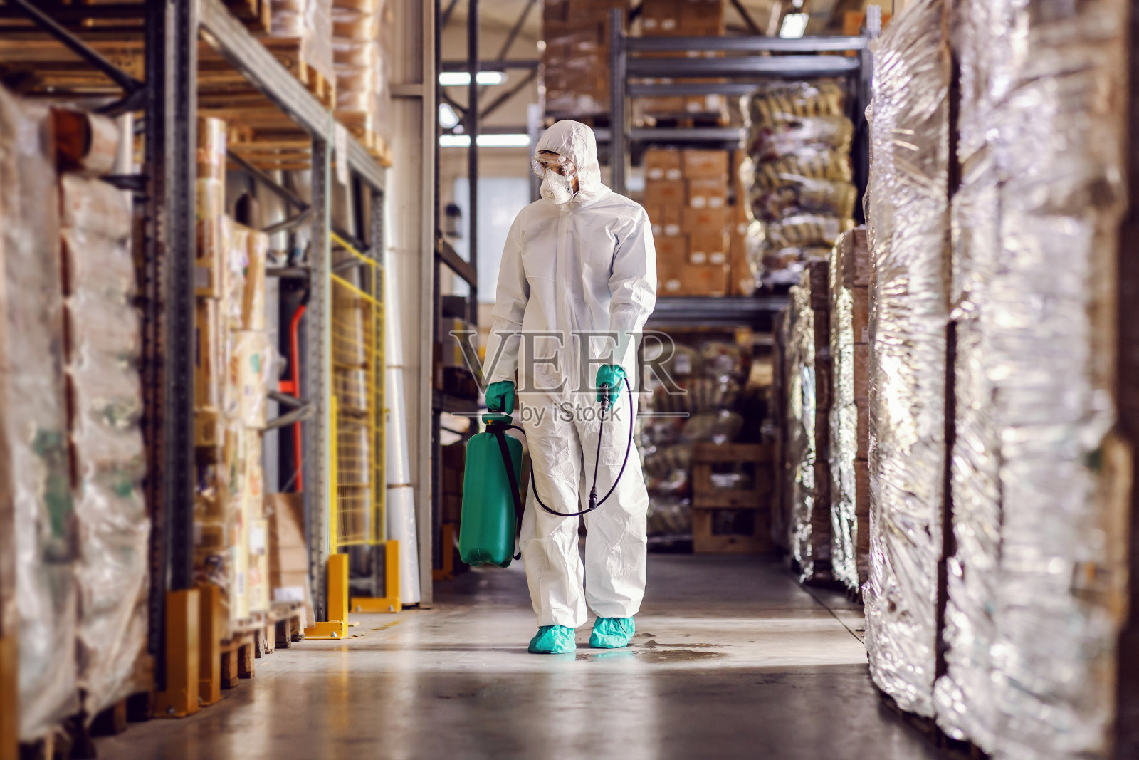 身着防护服和口罩的男子正在为装满冠状病毒/ covid-19食品的仓库进行消毒。照片摄影图片