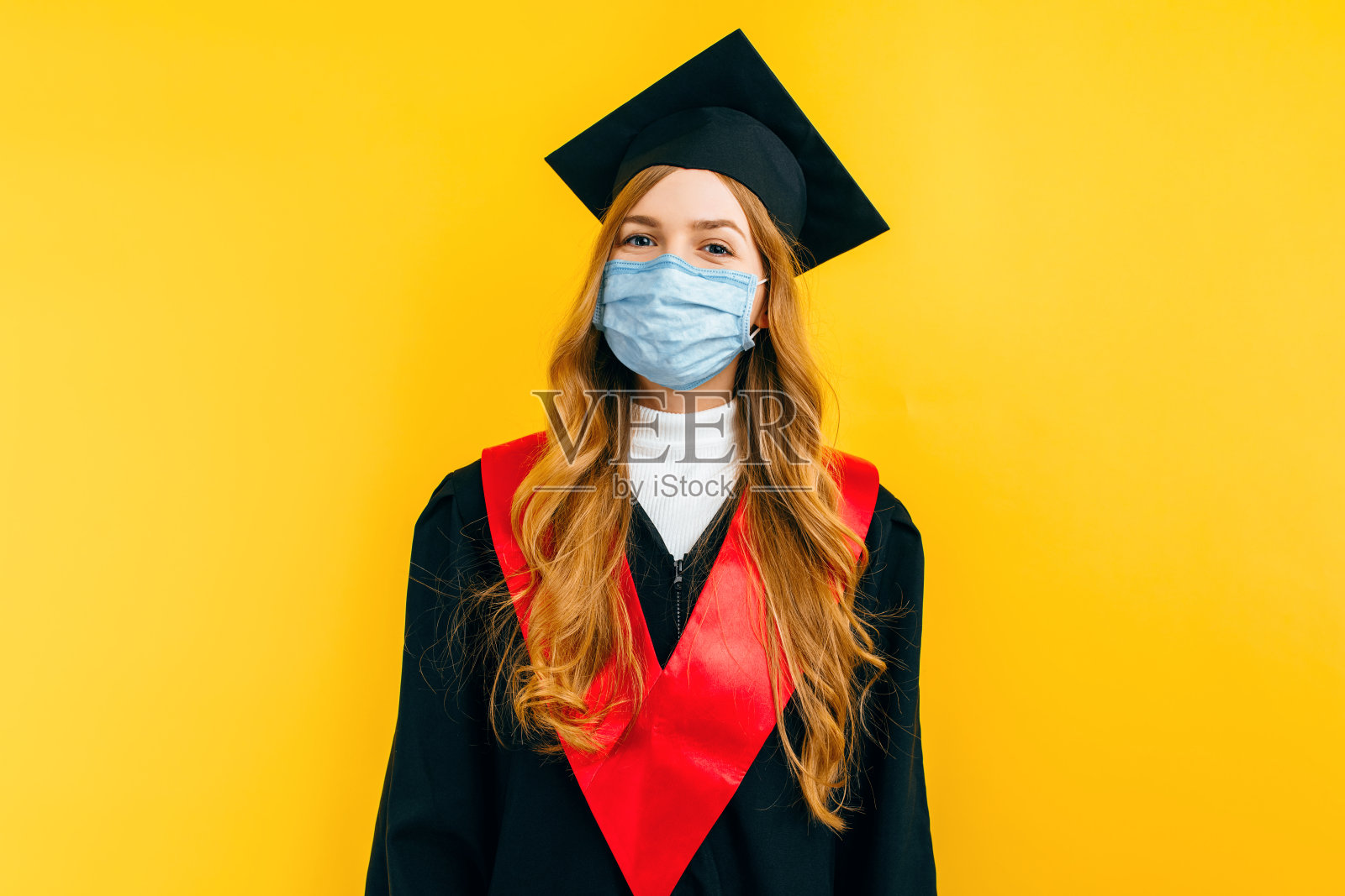 美丽的毕业女子戴着医用防护口罩在一个孤立的黄色背景。毕业,检疫,冠状病毒照片摄影图片