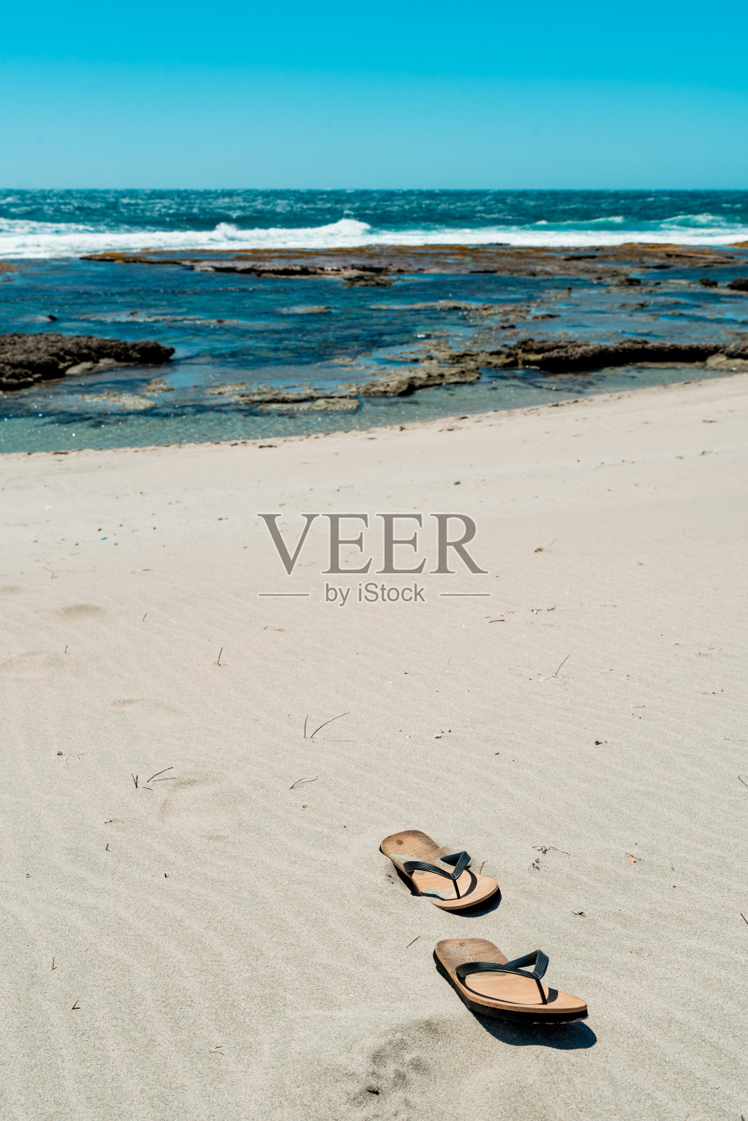 在海边的沙滩上穿着人字拖。背景是海浪。空的海滩照片摄影图片