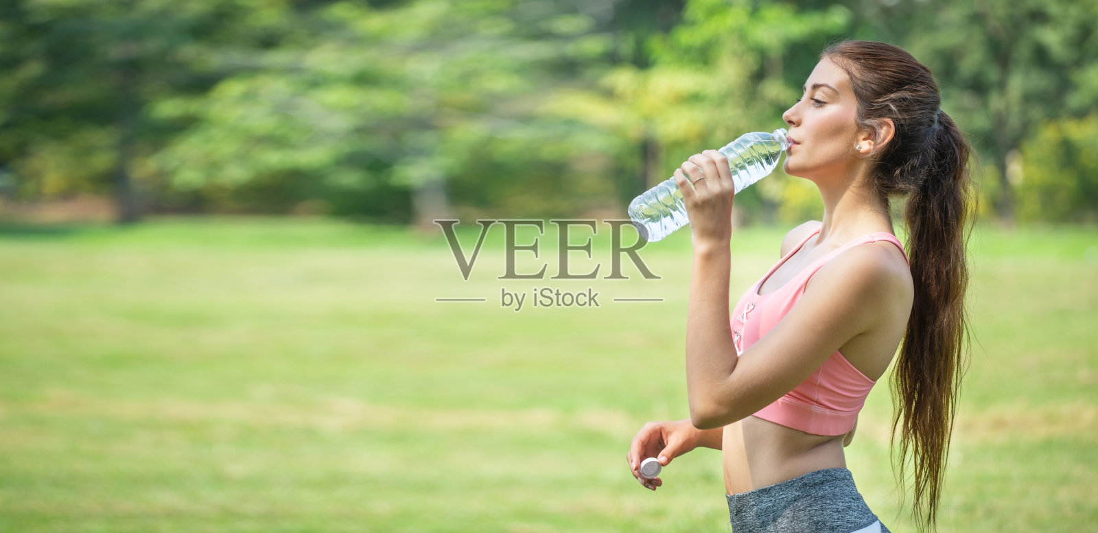 年轻的健身妇女饮用塑料瓶水后在公共公园早上。运动美丽的女孩口渴在训练中锻炼休息。全景横幅拷贝空间。照片摄影图片