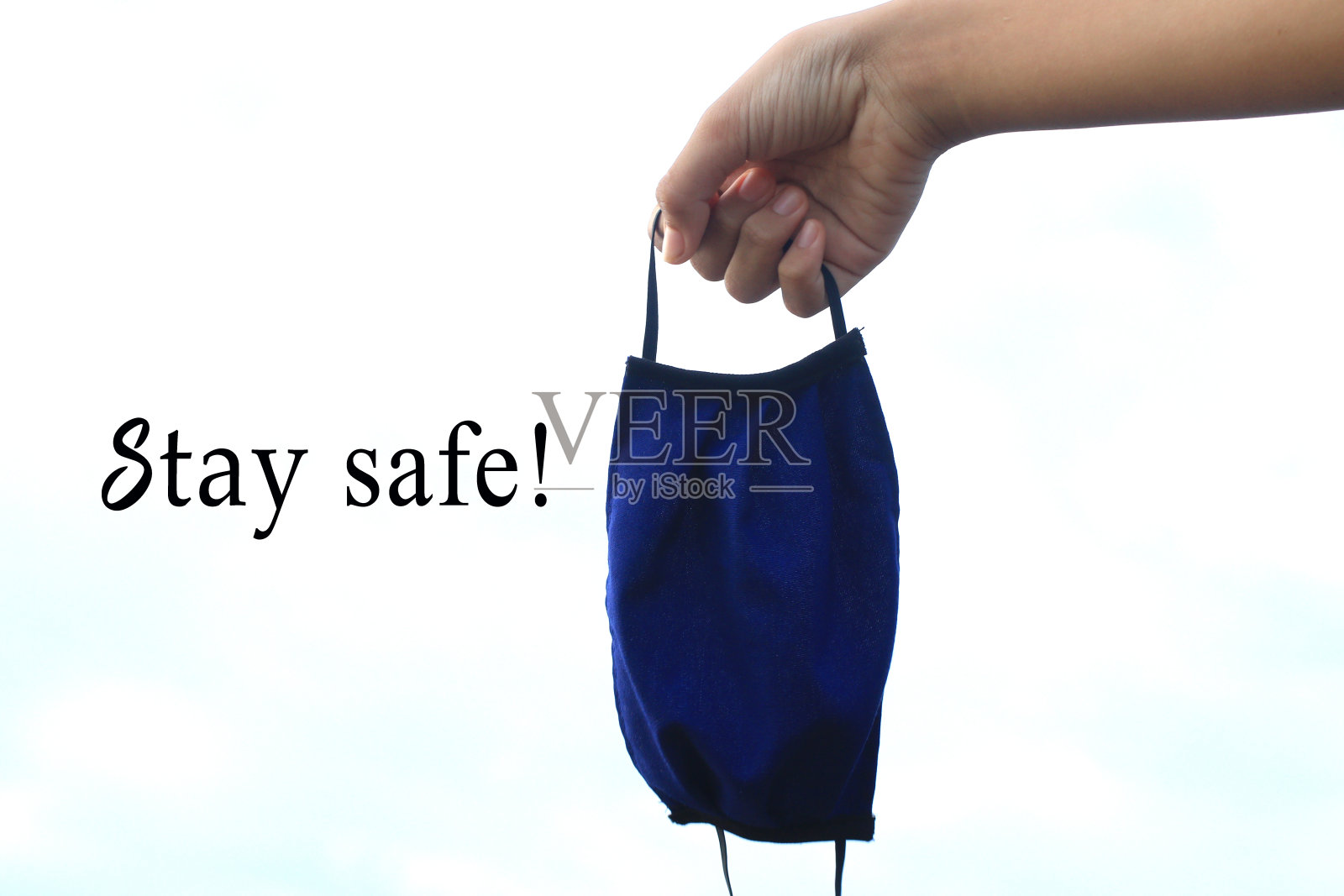 蓝色织物口罩在手白色背景与提醒信息-保持安全!照片摄影图片