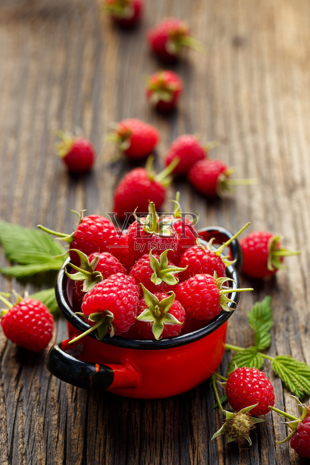 新鲜的覆盆子放在红色搪瓷锅里，放在质朴的木桌上照片摄影图片