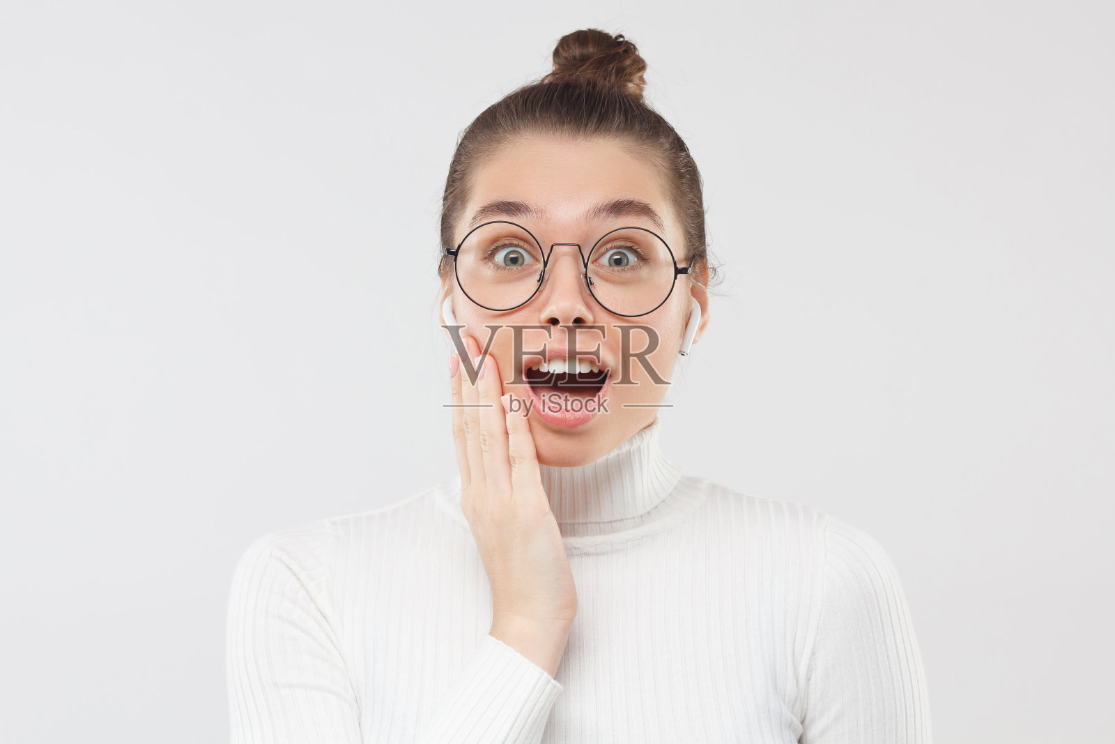 年轻的学生女孩在圆形眼镜感到兴奋和惊讶的大销售，看着与嘴张开，孤立在灰色的背景。OMG哇!照片摄影图片