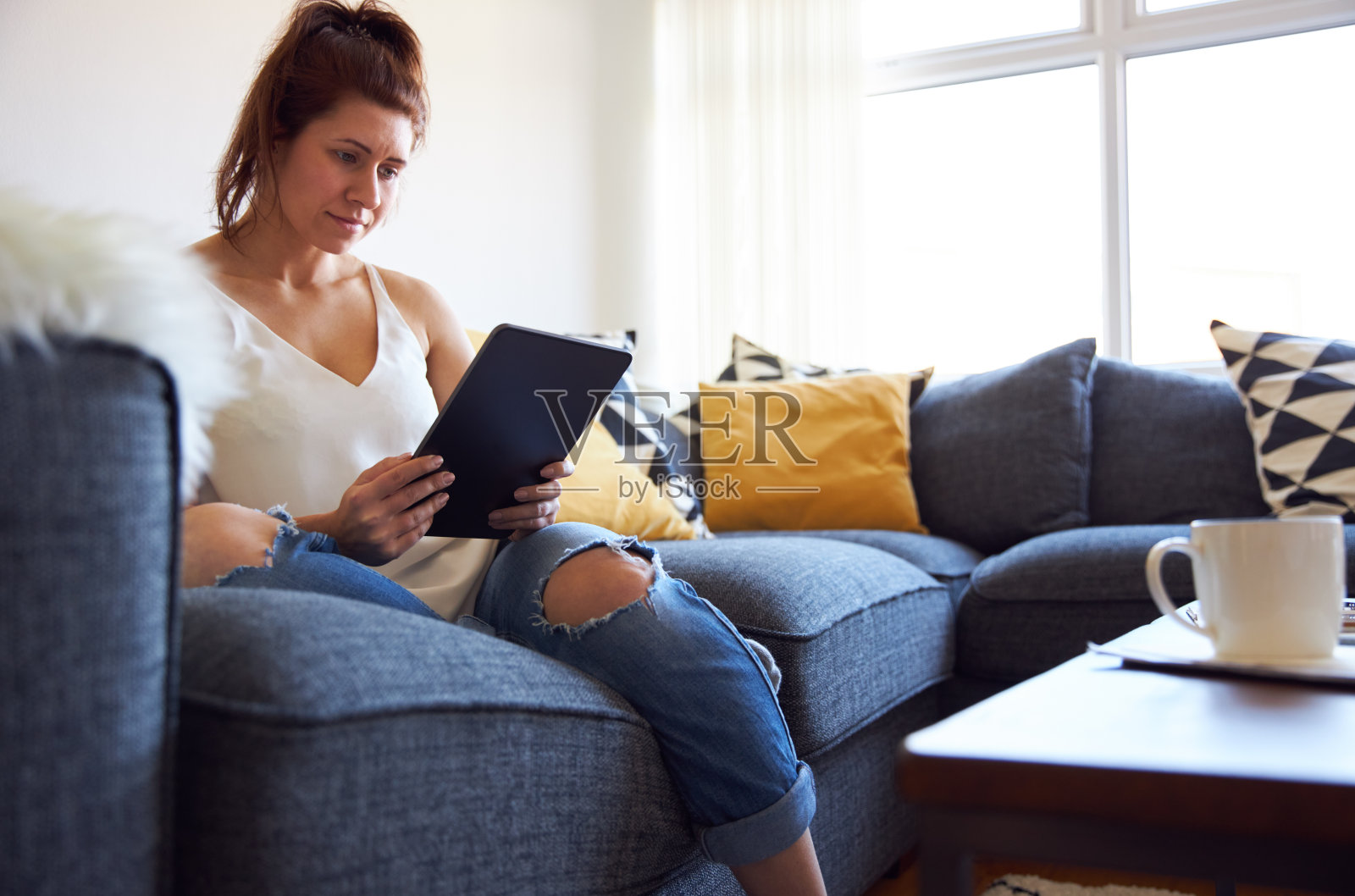 年轻女性坐在沙发上用平板电脑工作照片摄影图片