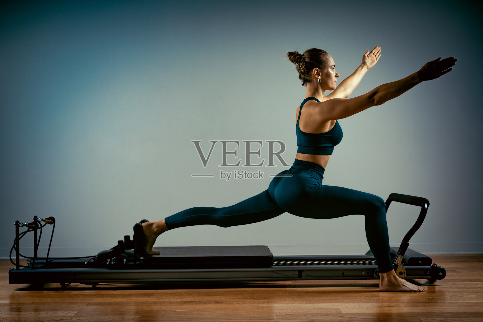 小女孩在床上做普拉提练习。美丽苗条的健身教练对改革者灰色背景，低调，艺术光。健康的概念照片摄影图片