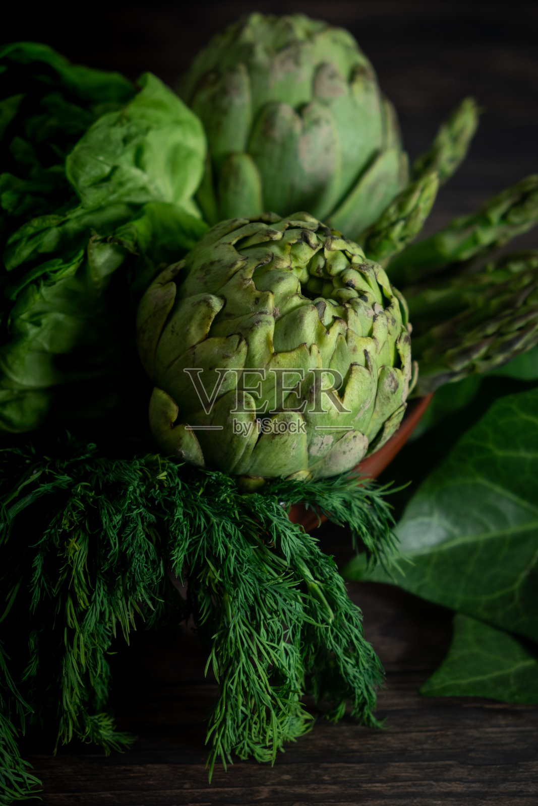 木桌上放着洋蓟、莴苣和香草。照片摄影图片