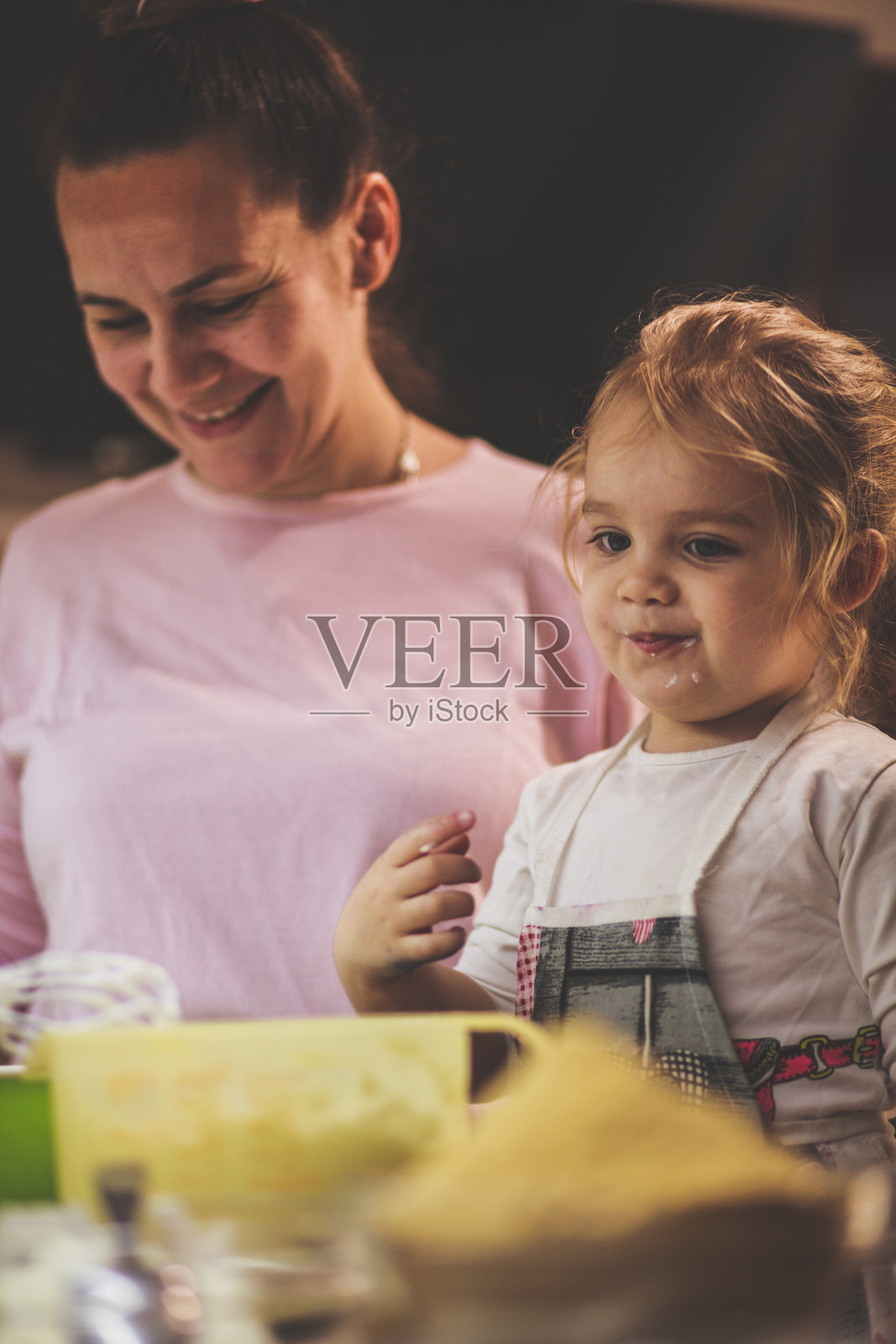 小女孩一边和妈妈做蛋糕，一边品尝面糊照片摄影图片