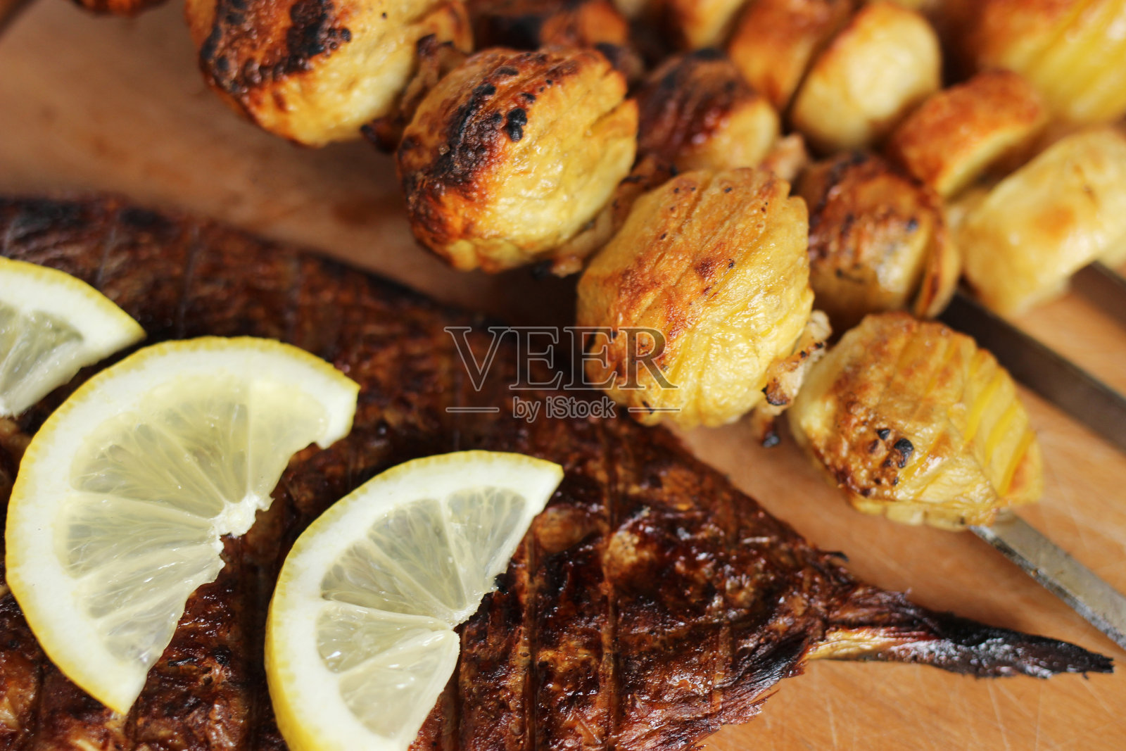 木桌上放着烤土豆、鱼和柠檬照片摄影图片