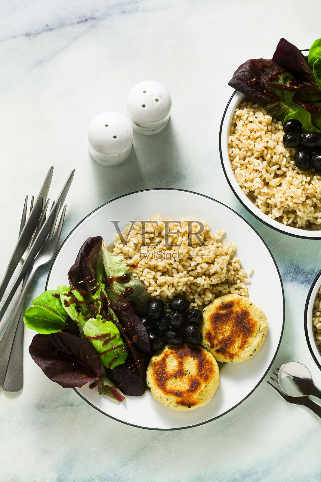 一个简单的素食午餐或晚餐为两个成年人和一个孩子的家庭。大理石桌上放着糙米、豆浆、土豆饼、新鲜沙拉和橄榄照片摄影图片