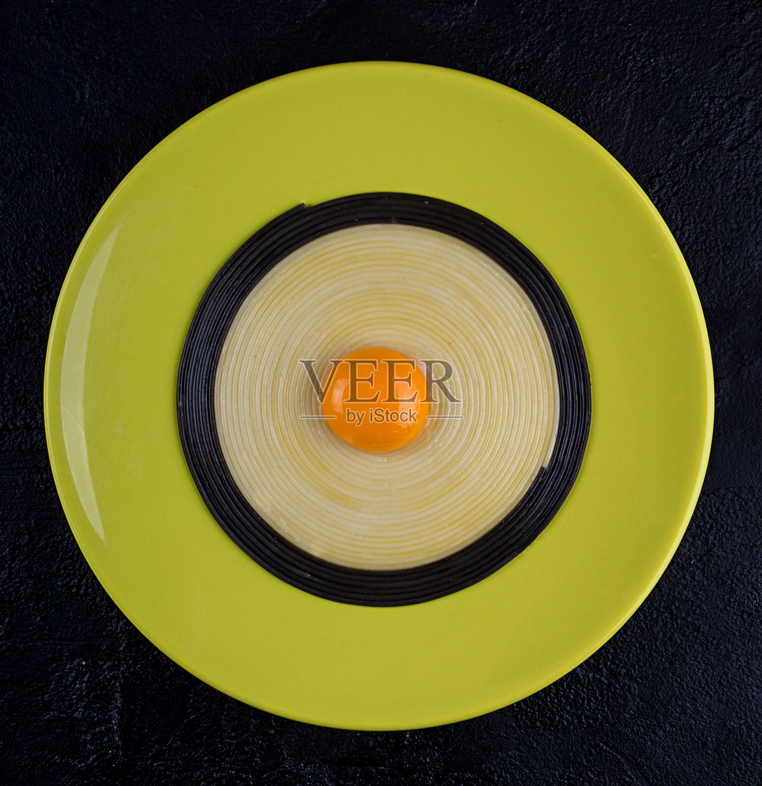 橄榄色的盘子，黑色的背景上，黑色和白色的扁意面中间是蛋黄。简约的风格。俯视图照片摄影图片