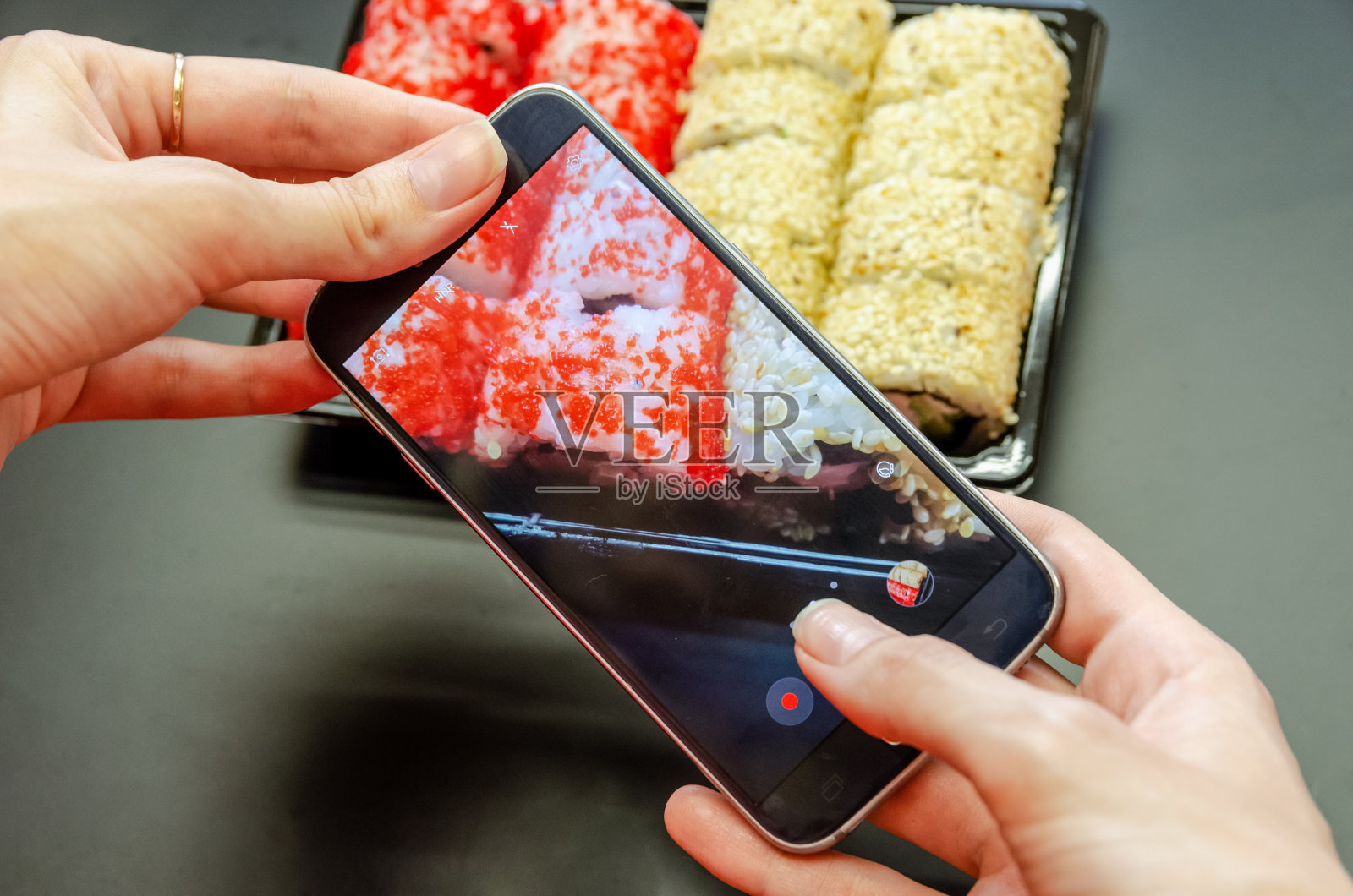 一个女孩用手机从不同的角度拍摄红白相间的寿司。特写照片。照片摄影图片