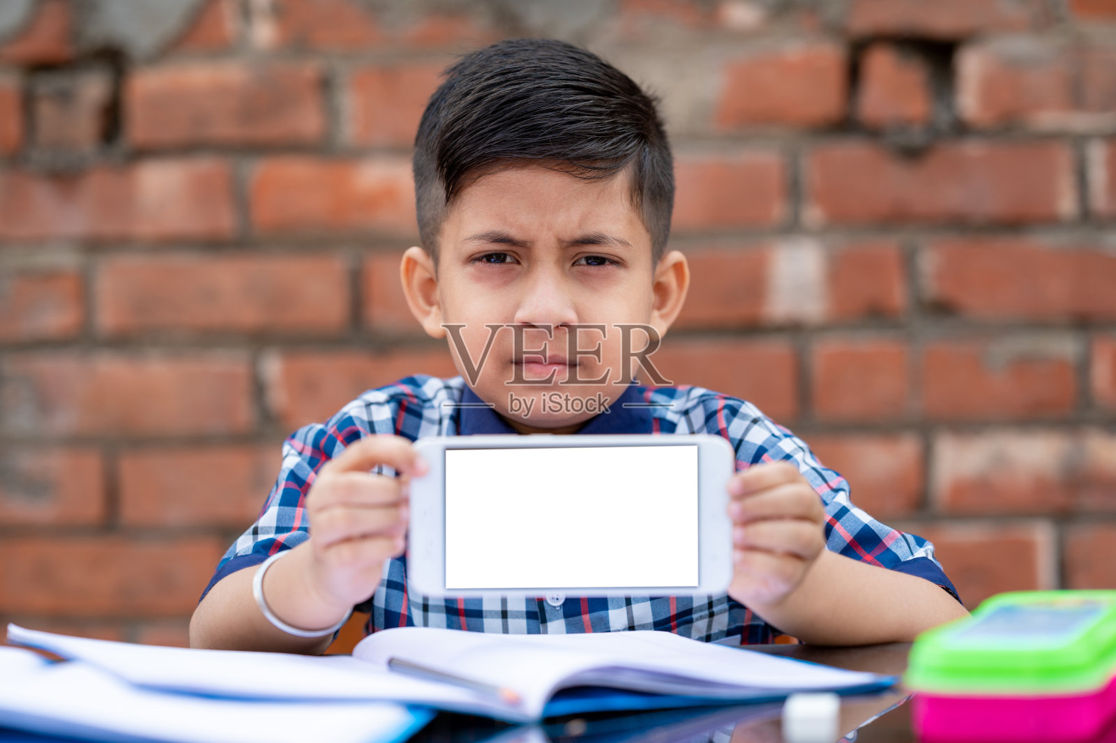 一个小学生在学习手机，他正在向相机展示他的手机。印度学校使用最新技术在学校学习。照片摄影图片