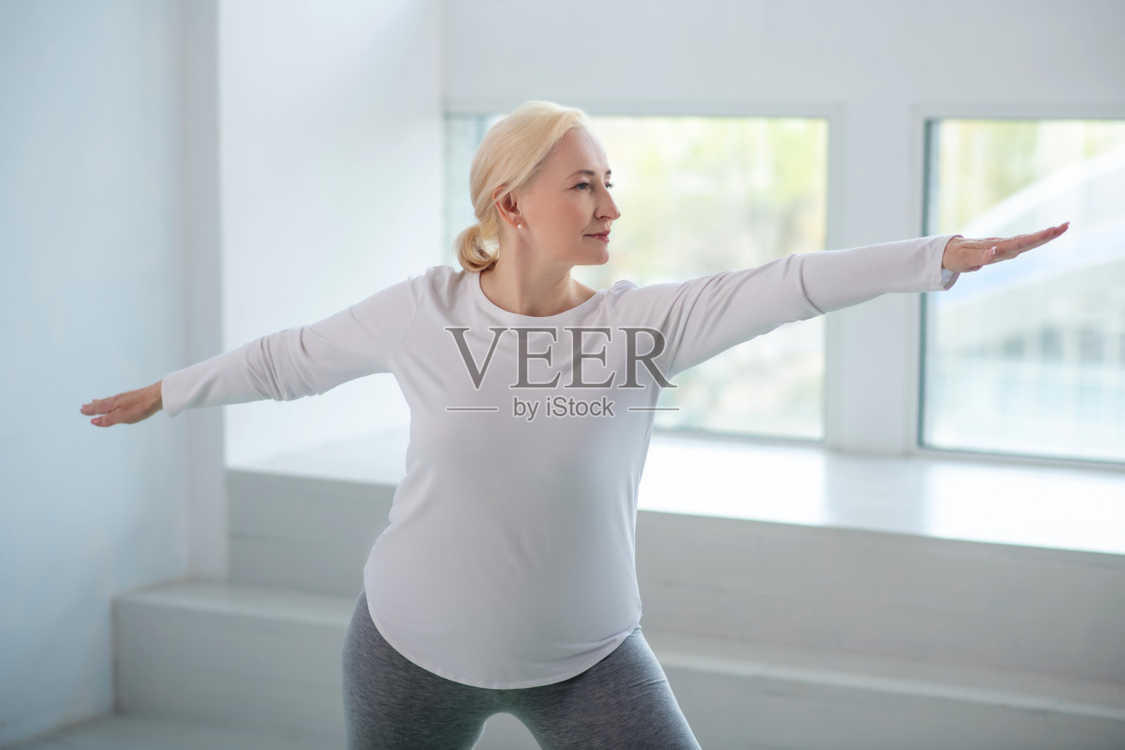 成熟的金发女性站在战士的姿势，手臂平行于地板照片摄影图片