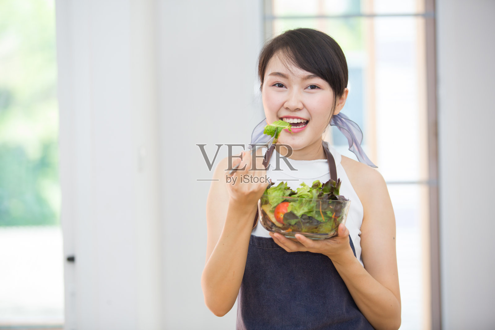 美丽的亚洲女人，美丽的笑容，健康的身体，美丽的牙齿，在家工作时吃沙拉蔬菜。照片摄影图片