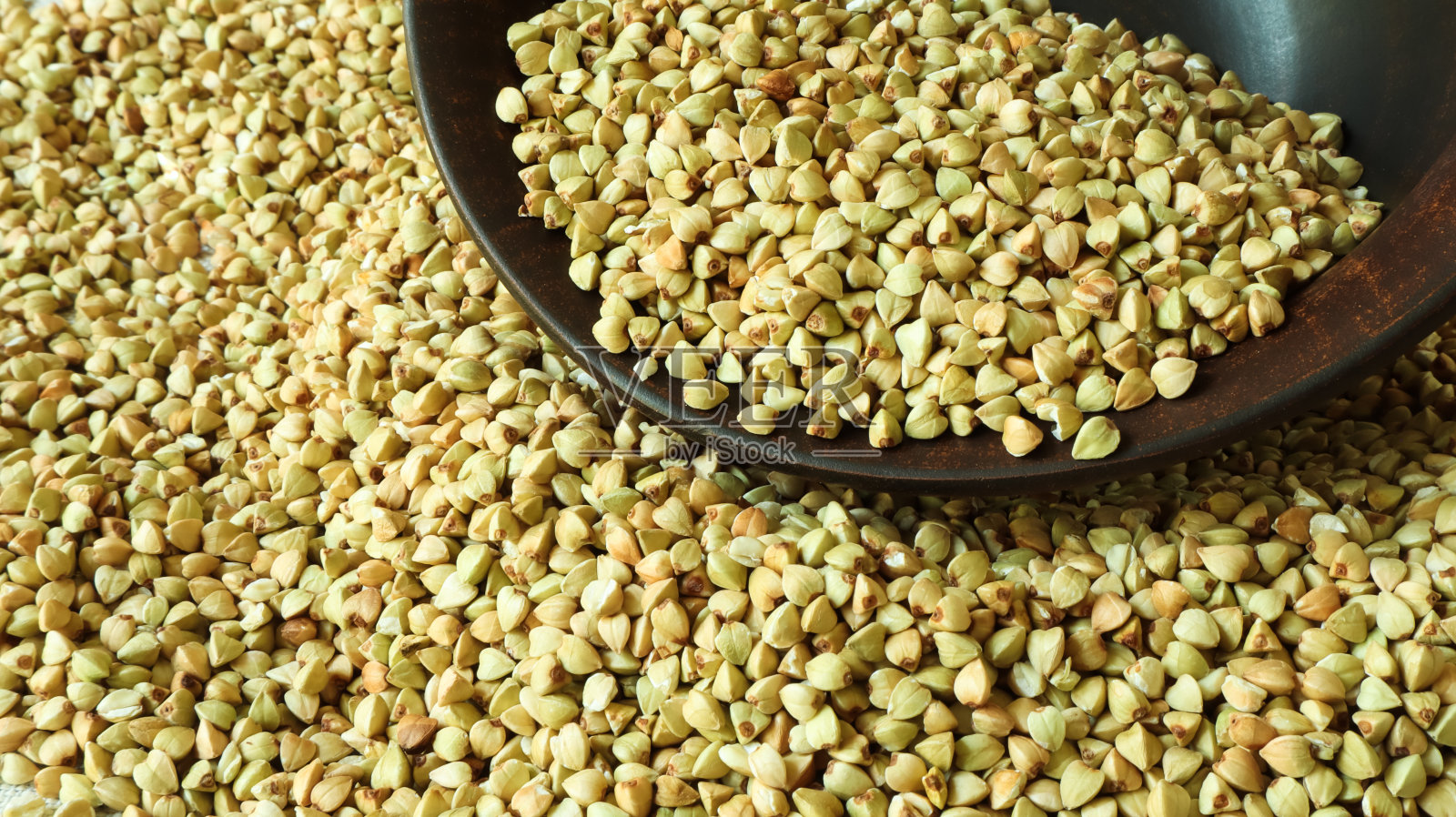 荞麦背景散落，生的绿色荞麦在一个棕色的粘土碗或盘子。健康的燕麦。有机生的非油炸素食。健康均衡饮食的概念。减肥食品照片摄影图片