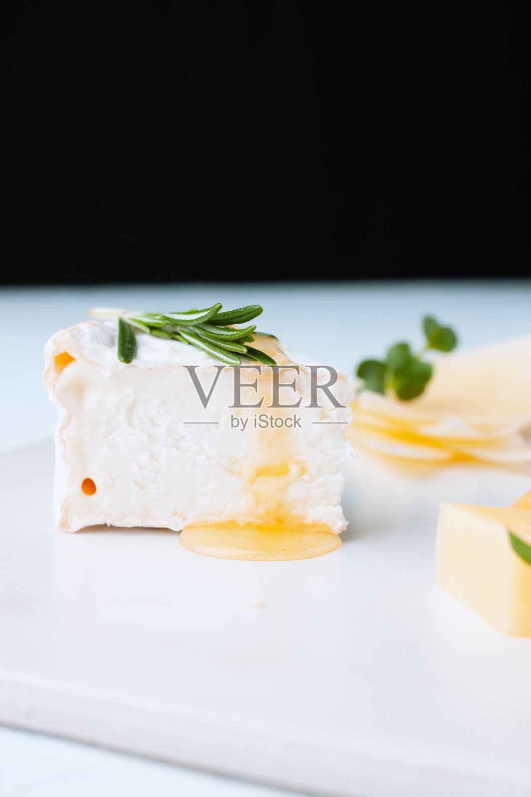 新鲜的自制蜂蜜和迷迭香奶酪配菜，背景是另一份奶酪盘。健康饮食概念-早餐加白软干酪或乳清干酪加蜂蜜照片摄影图片