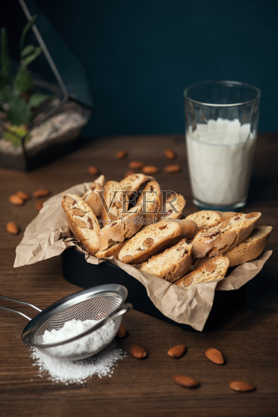 自制的带杏仁的意大利小甜饼装在金属盒里，放在棕色皱巴巴的纸上，配上一杯牛奶照片摄影图片