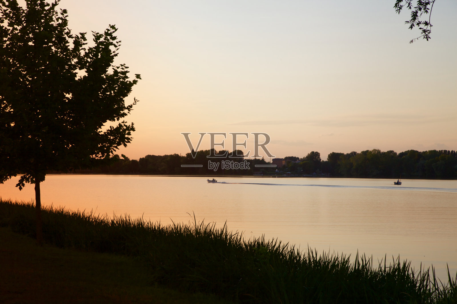 远处的湖岸和树林里有小船在水上，夕阳西下照片摄影图片