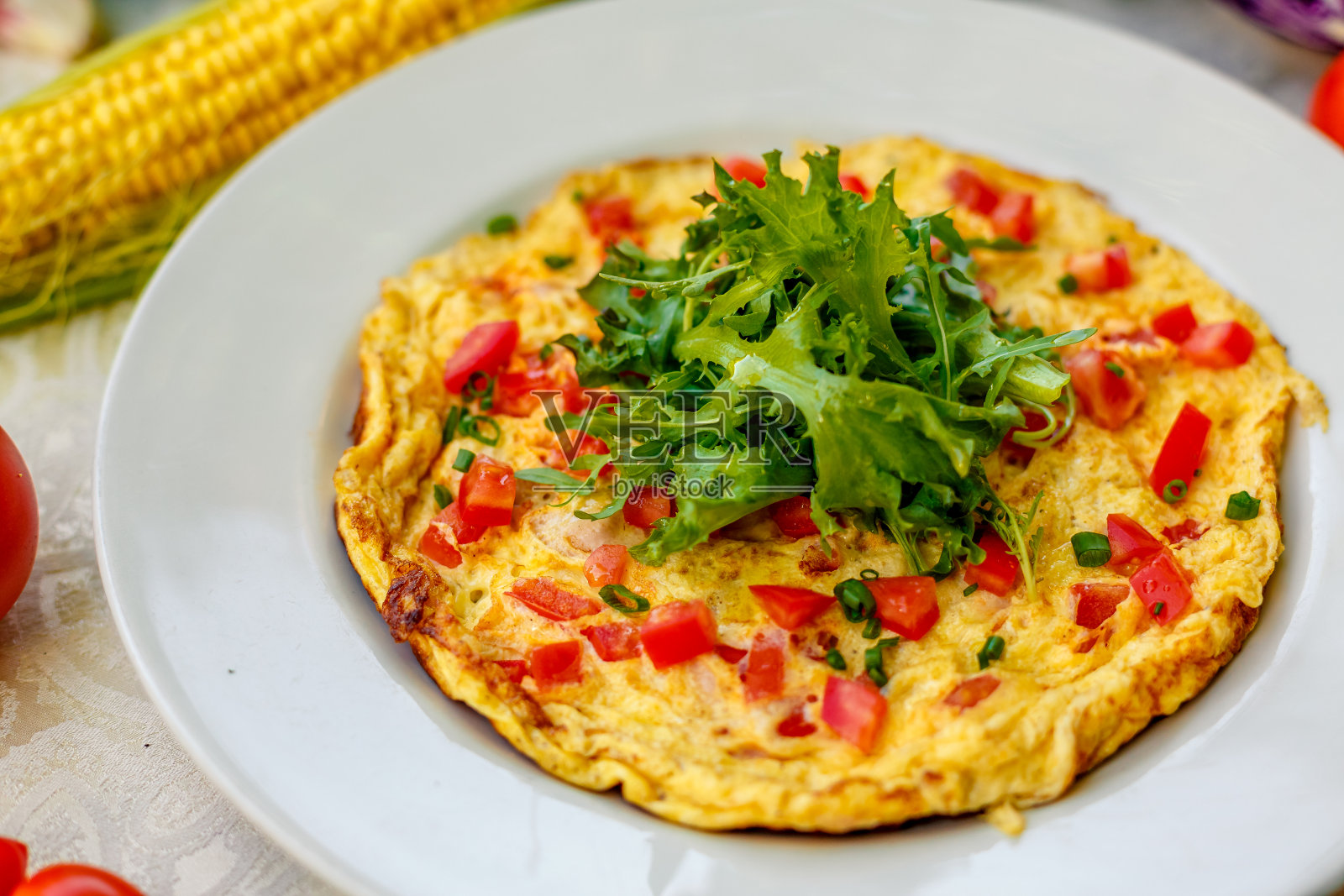 铺着白台布的桌子上放着鸡蛋煎蛋卷，上面放着圣女果、奶酪和芝麻菜照片摄影图片