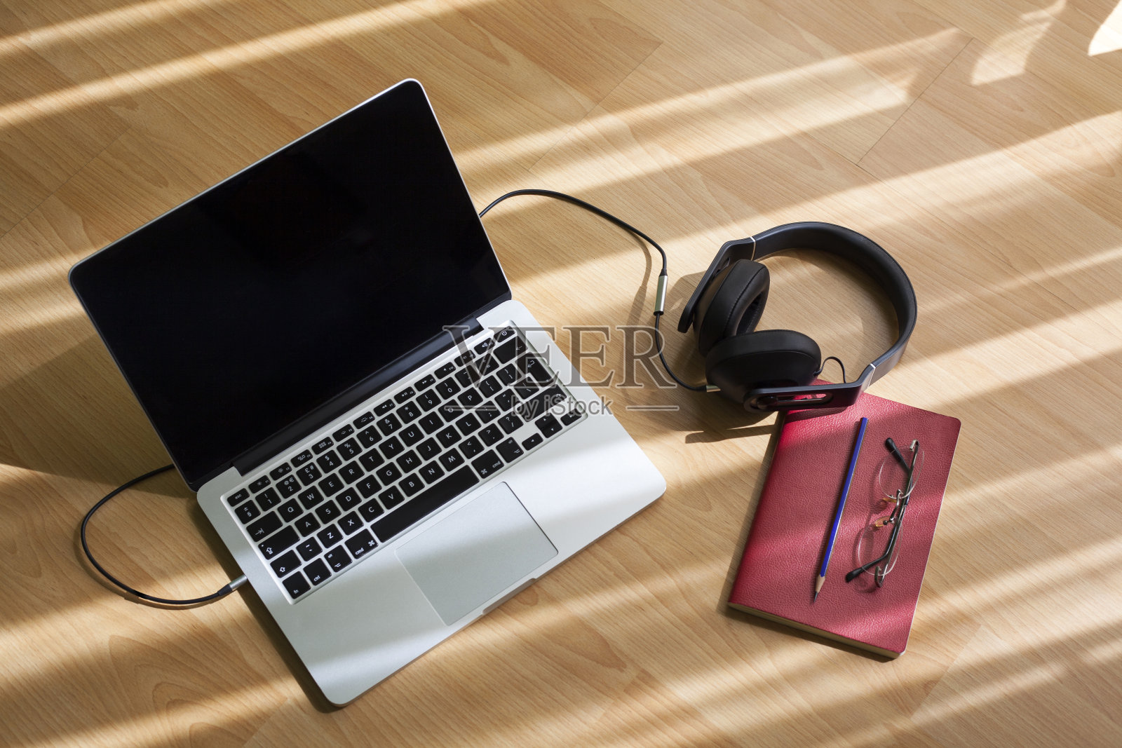 桌上放着笔记本电脑、笔、笔记本、眼镜和耳机。照片摄影图片