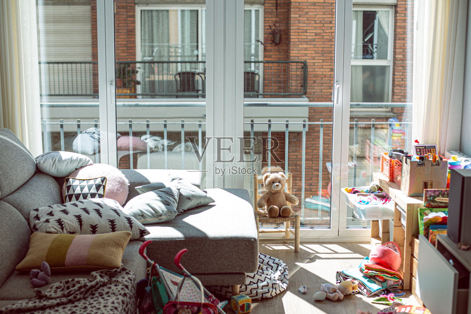 城市公寓的灰色沙发和地板上放着许多玩具的不整洁的休息室照片摄影图片