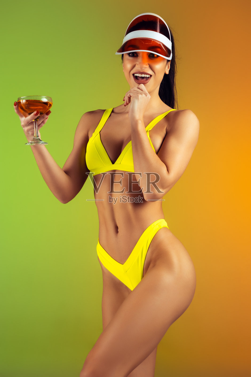 时尚肖像年轻的健康和运动的女人在时尚的黄色奢侈泳装在梯度背景鸡尾酒。完美的身材为夏天做好了准备。照片摄影图片