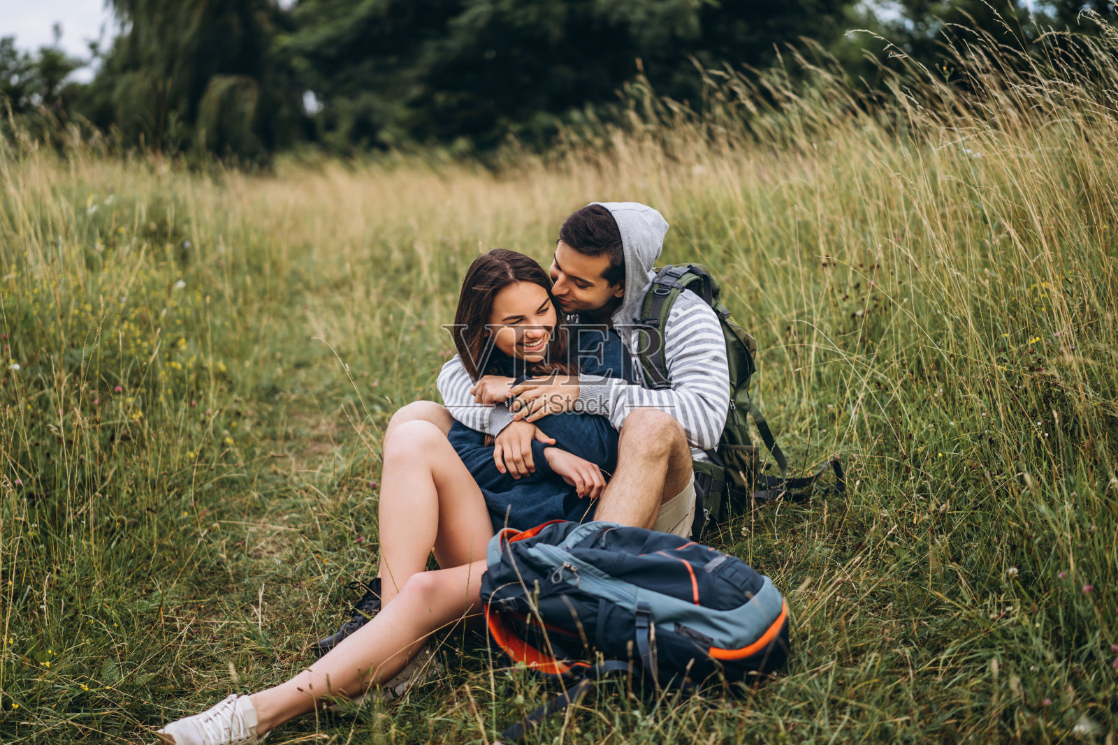 长发女子和背着背包坐在森林草地上的男子。享受大自然的乐趣，拥抱和亲吻照片摄影图片
