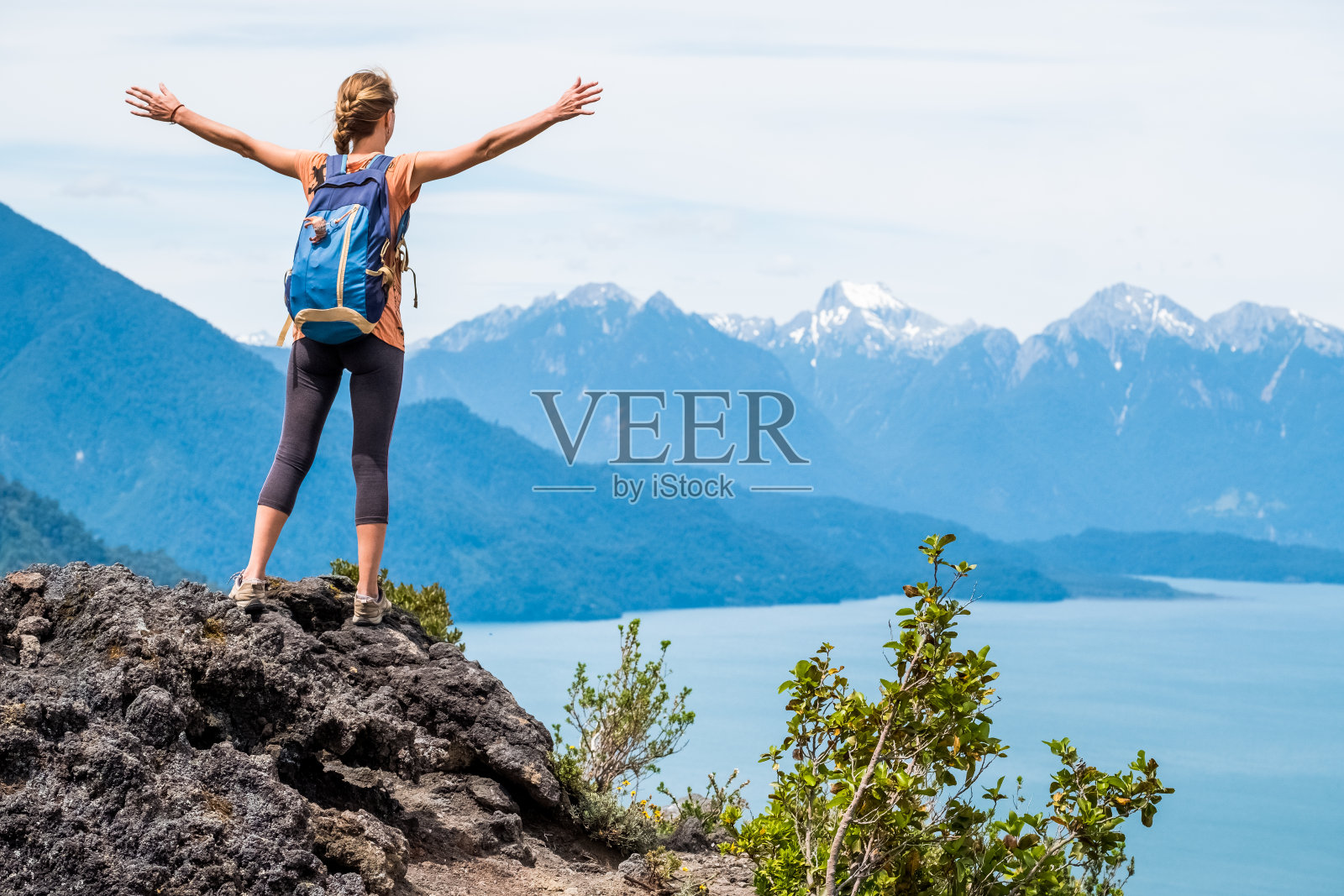 一位年轻的徒步旅行者站在岩石上，双手伸着，欣赏着山景照片摄影图片