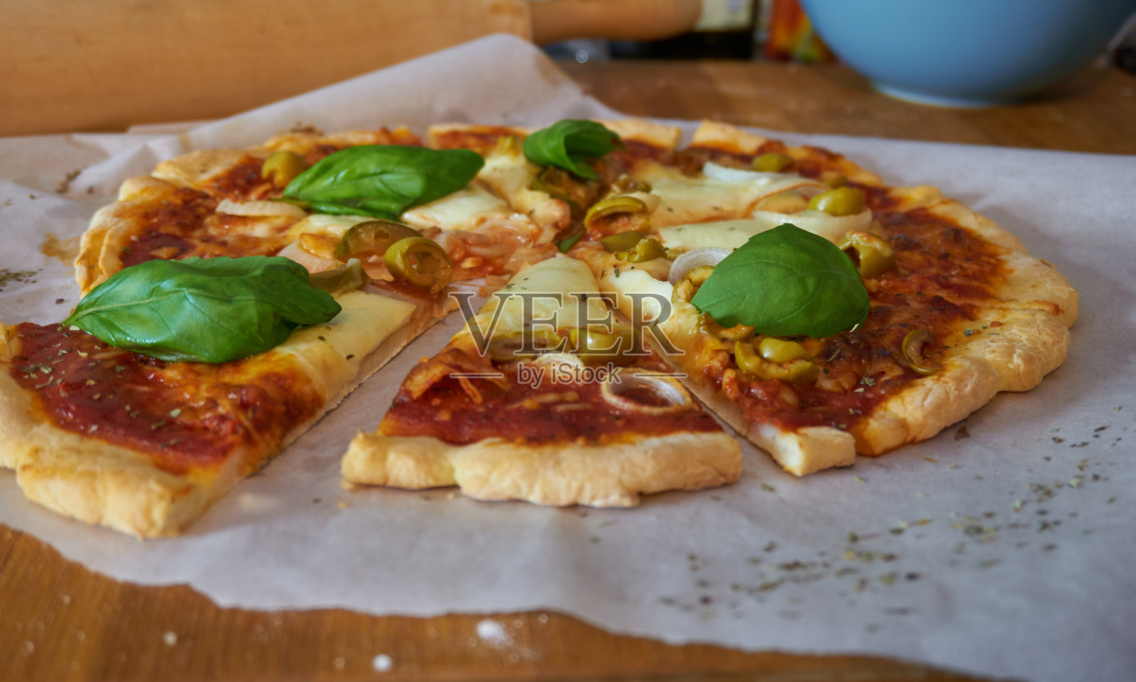 新鲜无麸质自制披萨，薄面团皮，橄榄，罗勒和洋葱，马苏里拉奶酪和番茄酱，在烤纸上照片摄影图片