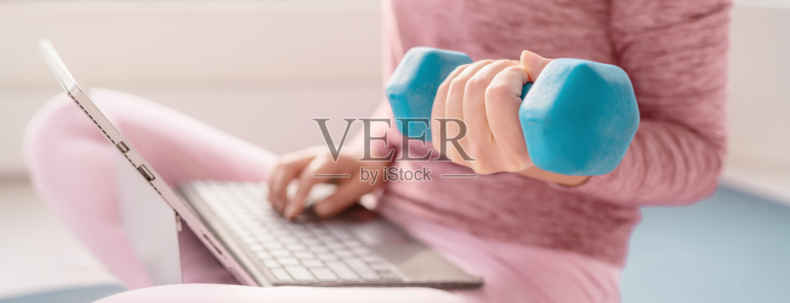 一个女人在家用笔记本电脑看在线健身视频，用哑铃练习健身课程。健身女孩使用重量锻炼手臂旗帜全景照片摄影图片