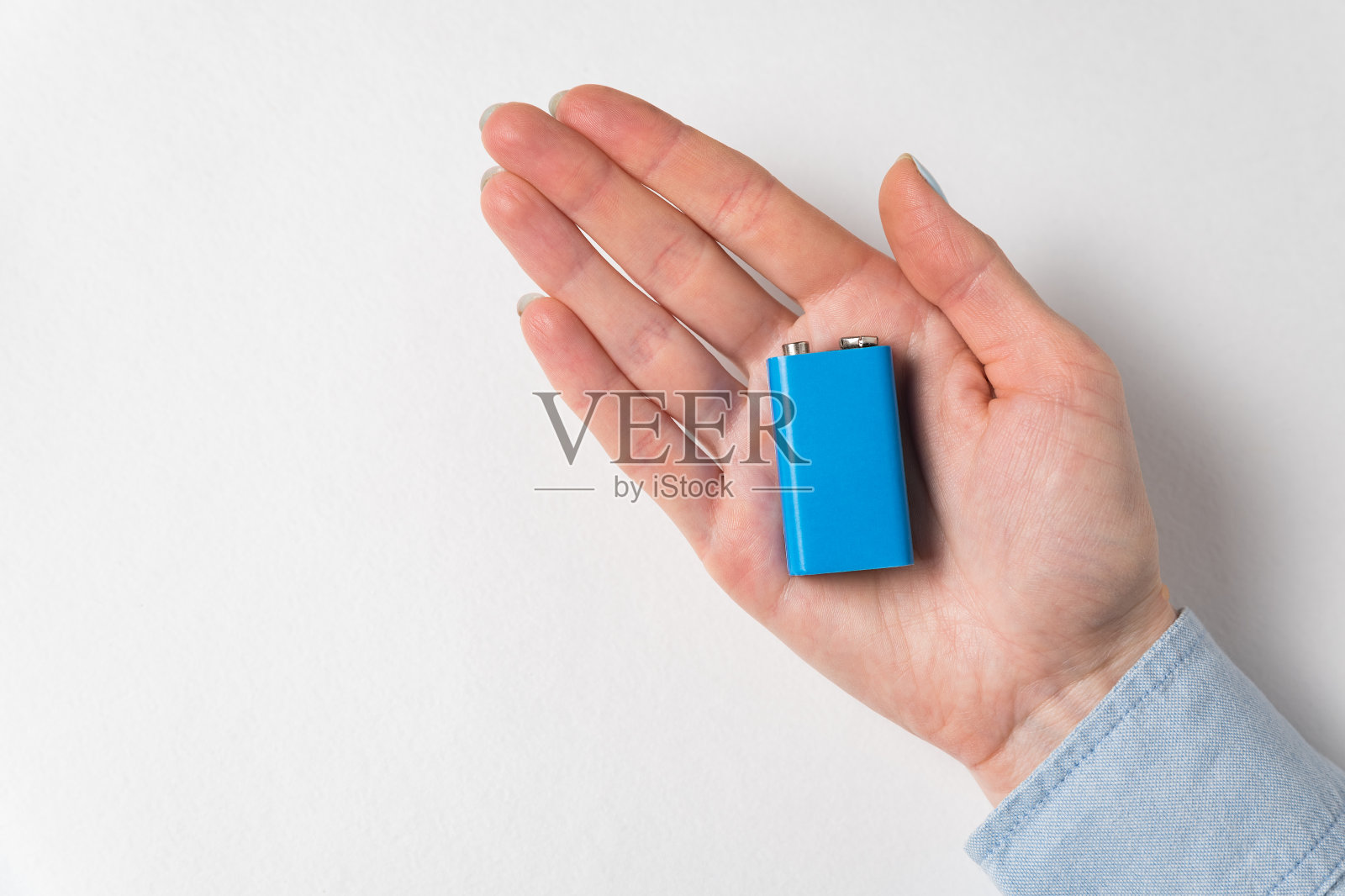 蓝色的PP3电池躺在女人的手掌上。蓄电池在白色背景照片摄影图片